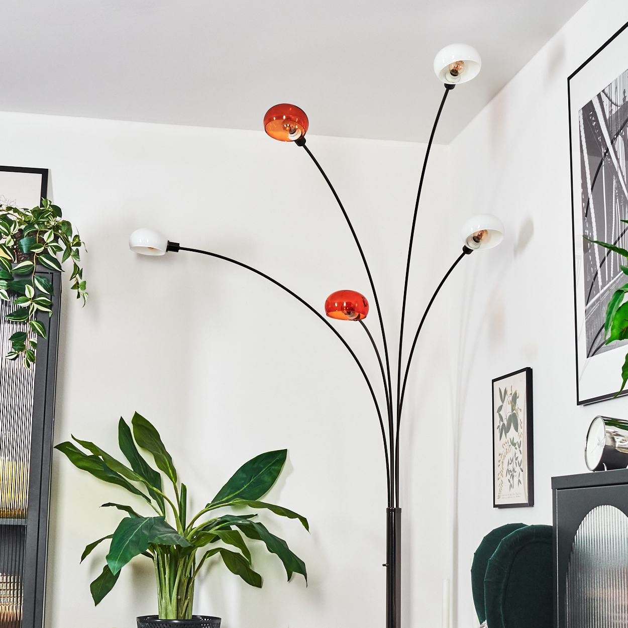 Eine moderne Stehlampe mit fünf orangefarbenen und weißen Glühbirnen. Davor steht eine große grüne Pflanze in einem Topf.