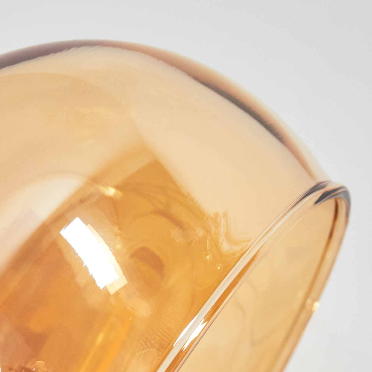 Nahaufnahme einer Glasschale. Die Schale ist bernsteinfarben und reflektiert Licht. Der Hintergrund ist weiß.