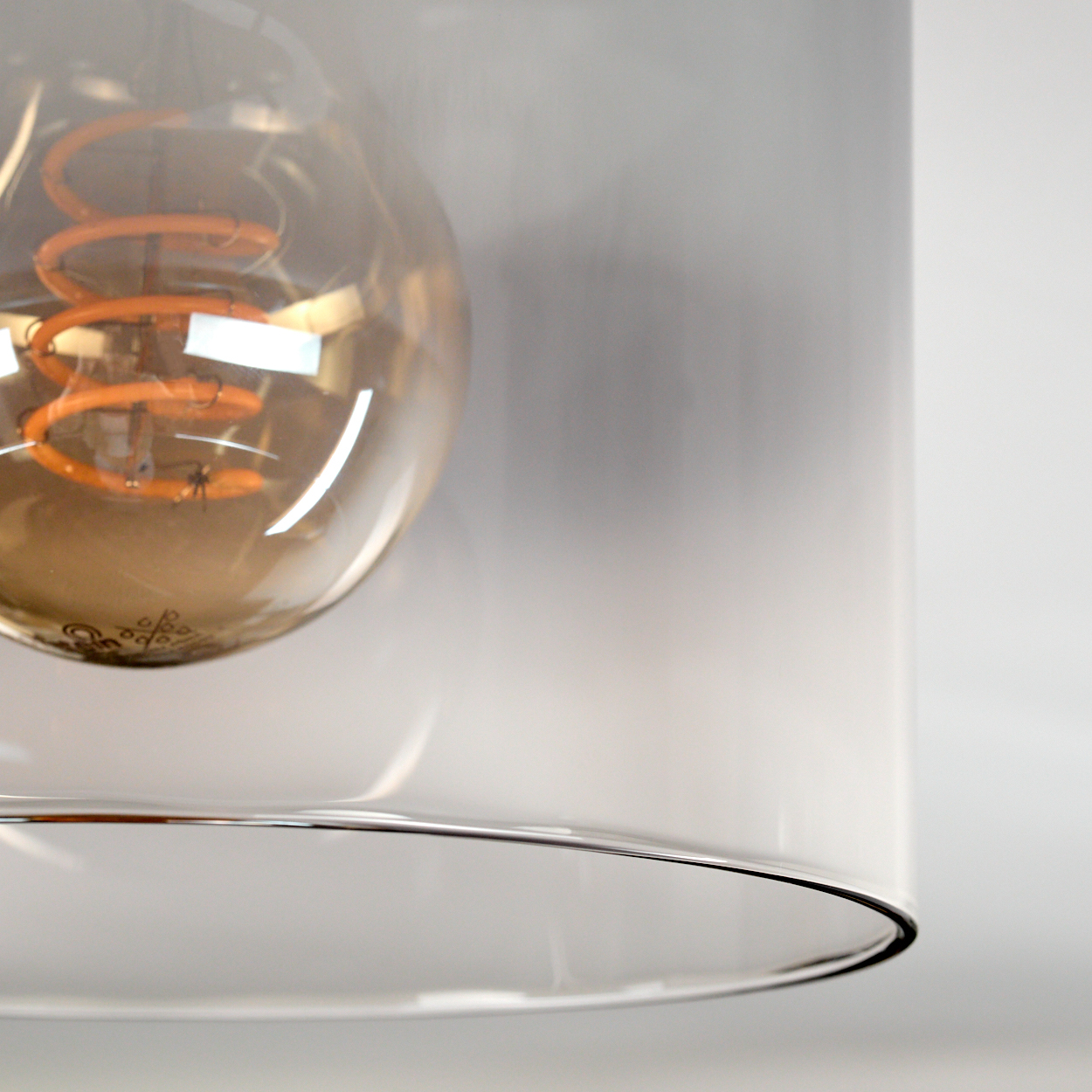 Nahaufnahme einer Leuchte. Ein Glasschirm umgibt eine Glühbirne mit einem orangefarbenen Glühfaden. Der Hintergrund ist eine weiße Wand.