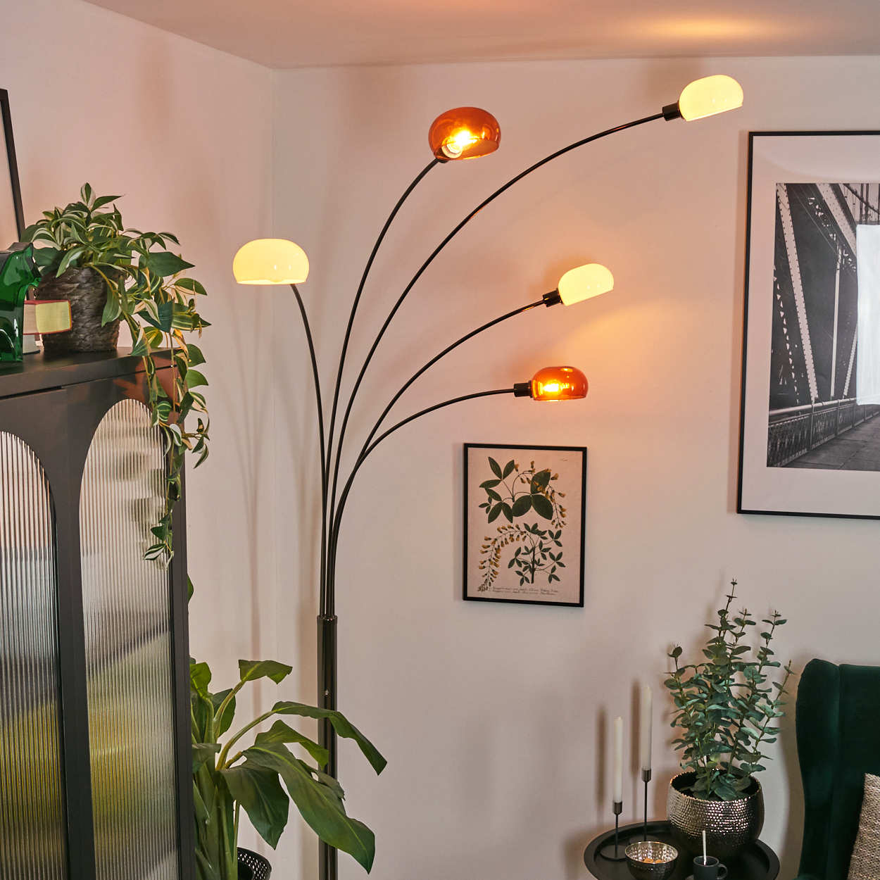 Ein modernes Wohnzimmer mit Stehlampe, Pflanzen und gerahmter Kunst. Die Lampe hat mehrere Lichter, einige bernsteinfarben und einige weiß.