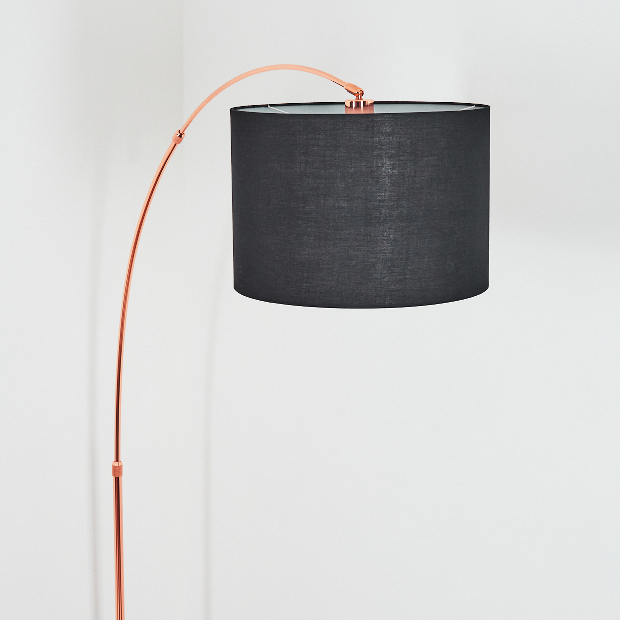 Eine moderne Stehlampe mit schwarzem Lampenschirm und kupferfarbenem Metallrahmen steht vor einer weißen Wand.