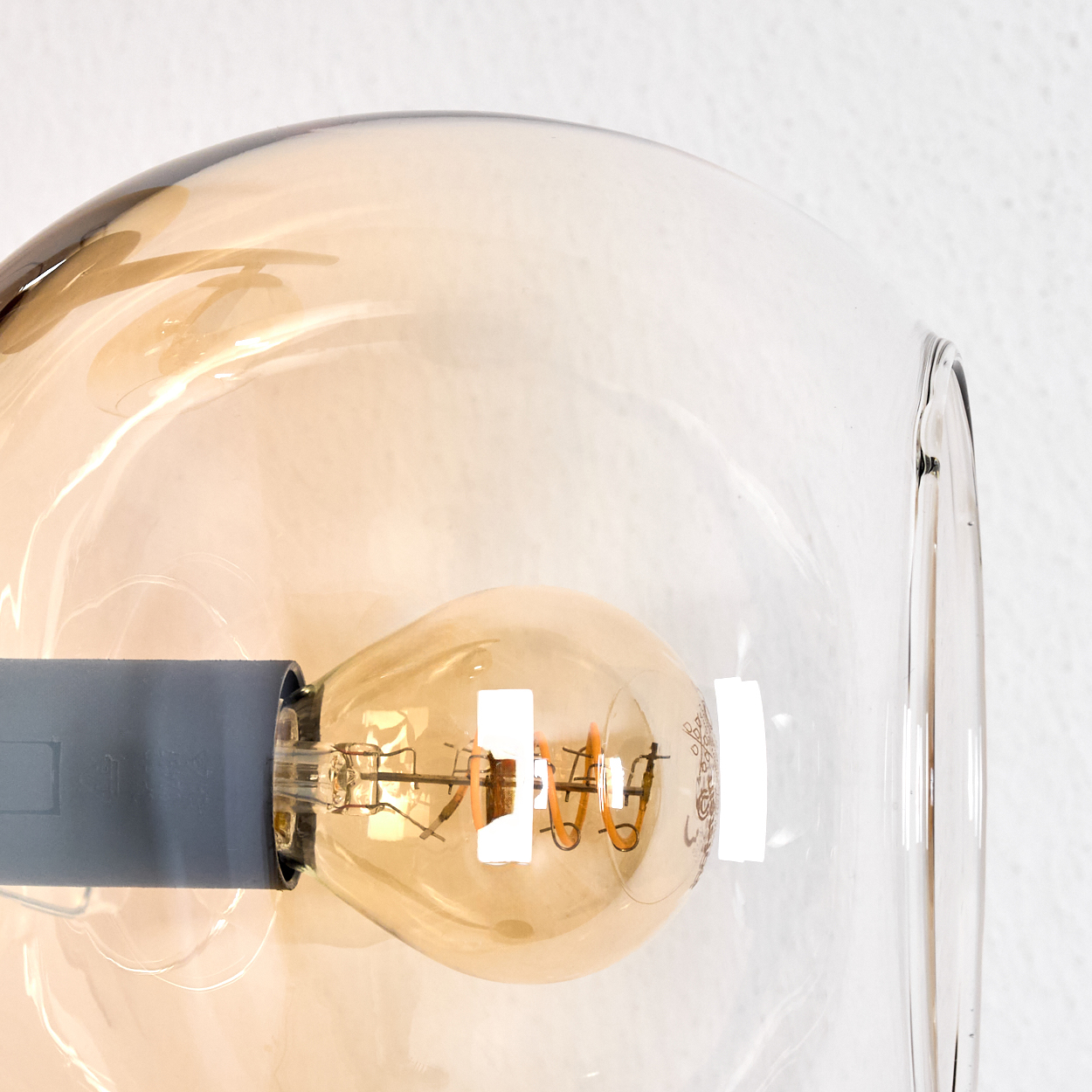 Nahaufnahme einer Glühbirne in einer Glaskugel. Die Glühbirne leuchtet warm. Der Hintergrund ist eine weiße Wand.