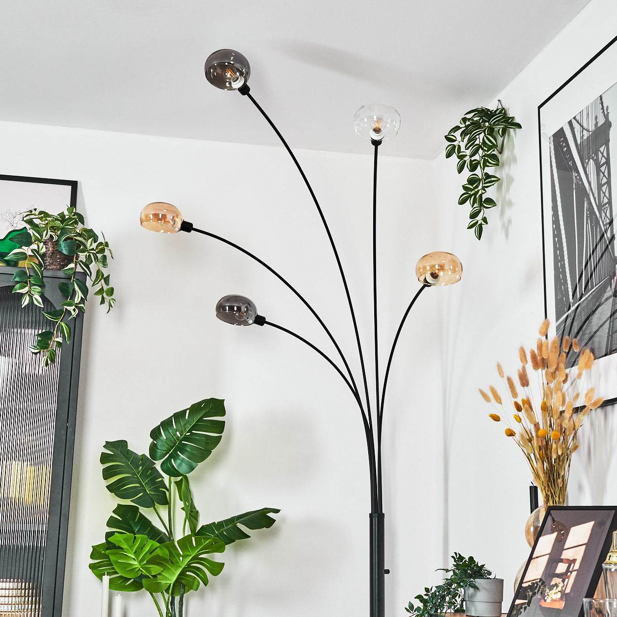 Eine moderne Stehlampe mit fünf Kugellampen. Grüne Pflanzen und ein gerahmtes Bild schmücken den Raum mit weißen Wänden.