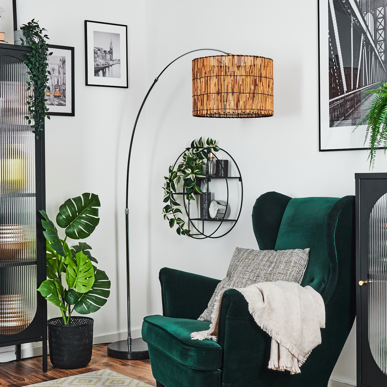 Wohnzimmer mit grünem Sessel, Stehlampe, Pflanzen und gerahmten Bildern an einer weißen Wand. Gemütliche und stilvolle Einrichtung.