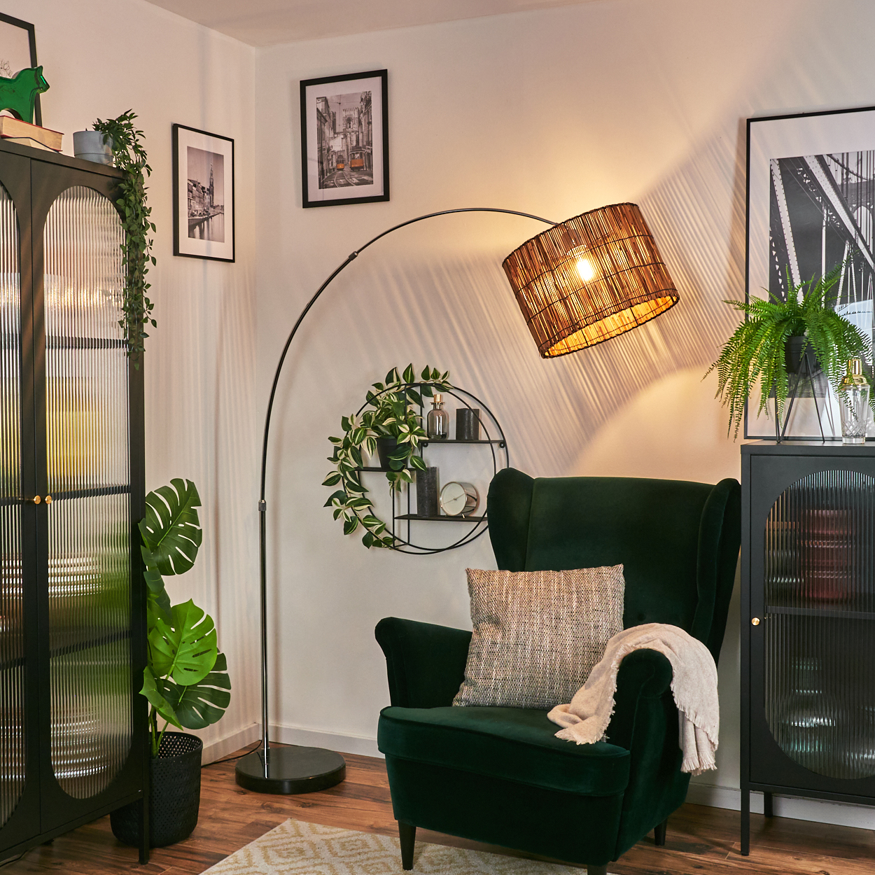 Ein grüner Sessel mit Kissen und Decke, eine Lampe, ein schwarzer Schrank und gerahmte Bilder an der Wand.