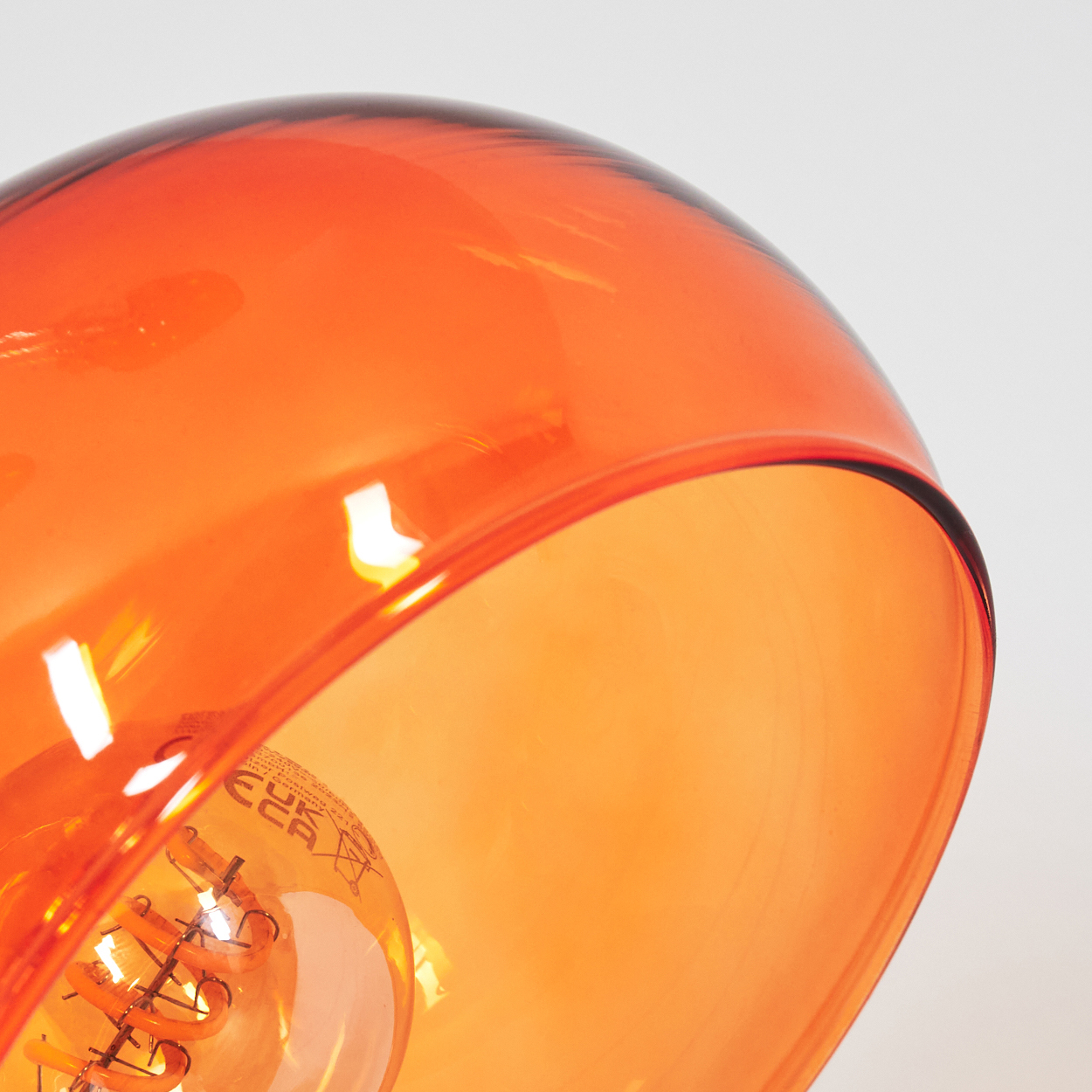 Nahaufnahme eines orangenen Glasschirms mit einer sichtbaren Glühbirne im Inneren. Der Hintergrund ist weiß.