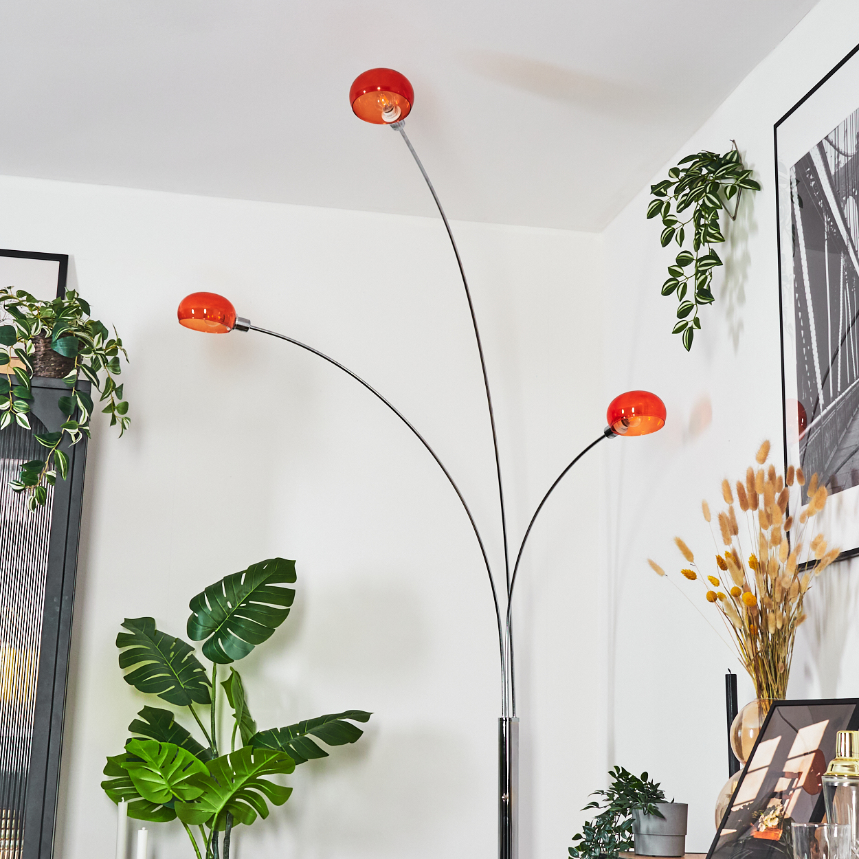 Eine moderne Stehlampe mit drei orangefarbenen Kugelleuchten. Pflanzen und Kunstwerke im Hintergrund, ein stilvolles Interieur.