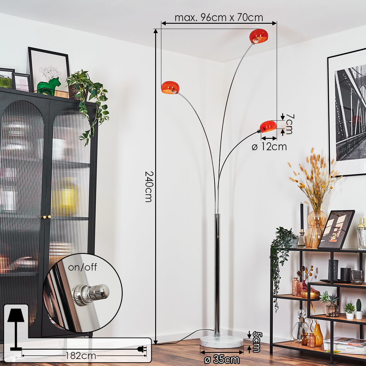 Eine hohe Stehlampe mit drei orangefarbenen Lampenschirmen. Die Lampe steht neben einem schwarzen Schrank und einem Regal mit Dekorationen.