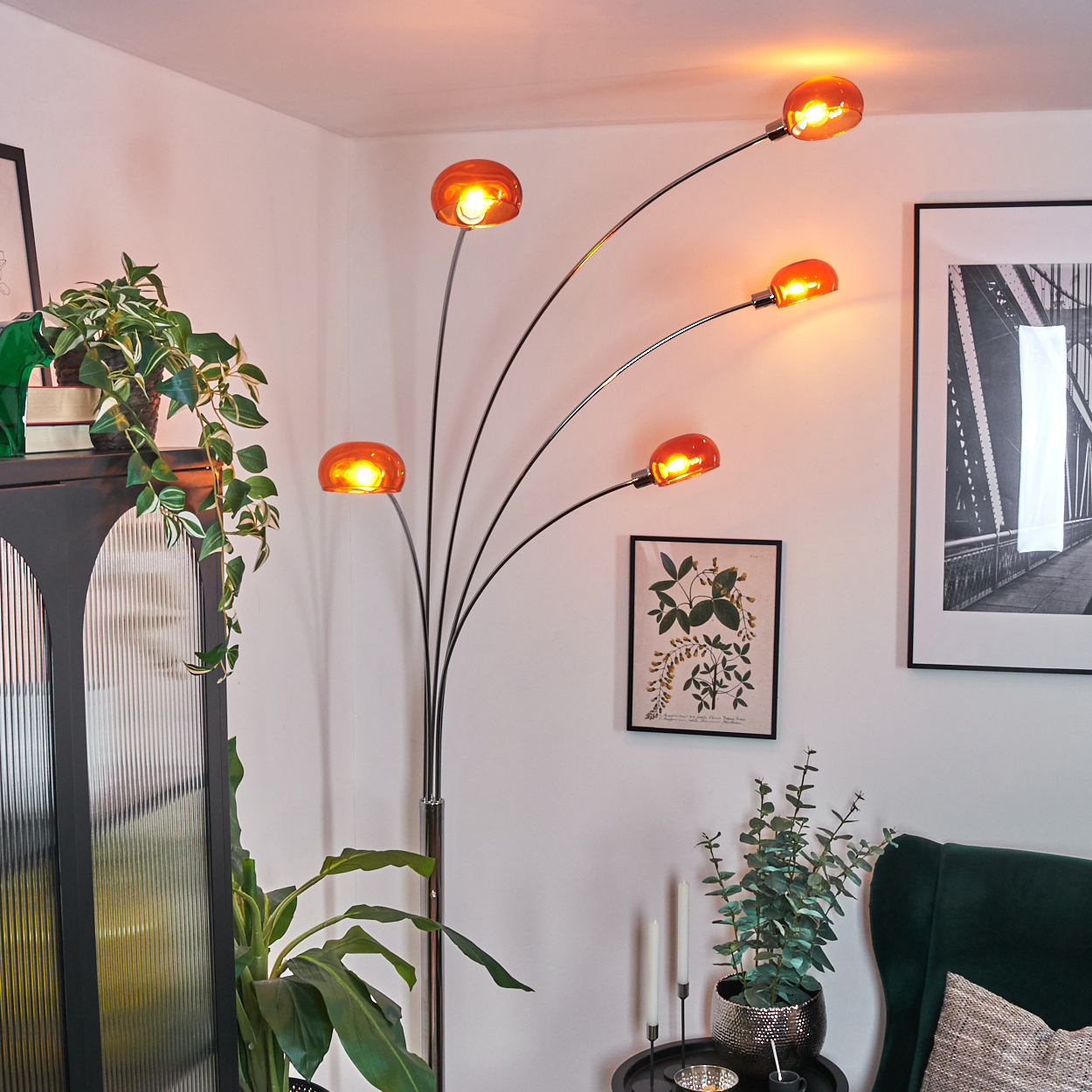 Ein modernes Wohnzimmer mit einer Stehlampe mit orangefarbenen Glühbirnen. Grüne Pflanzen und ein dunkler Schrank im Vordergrund.