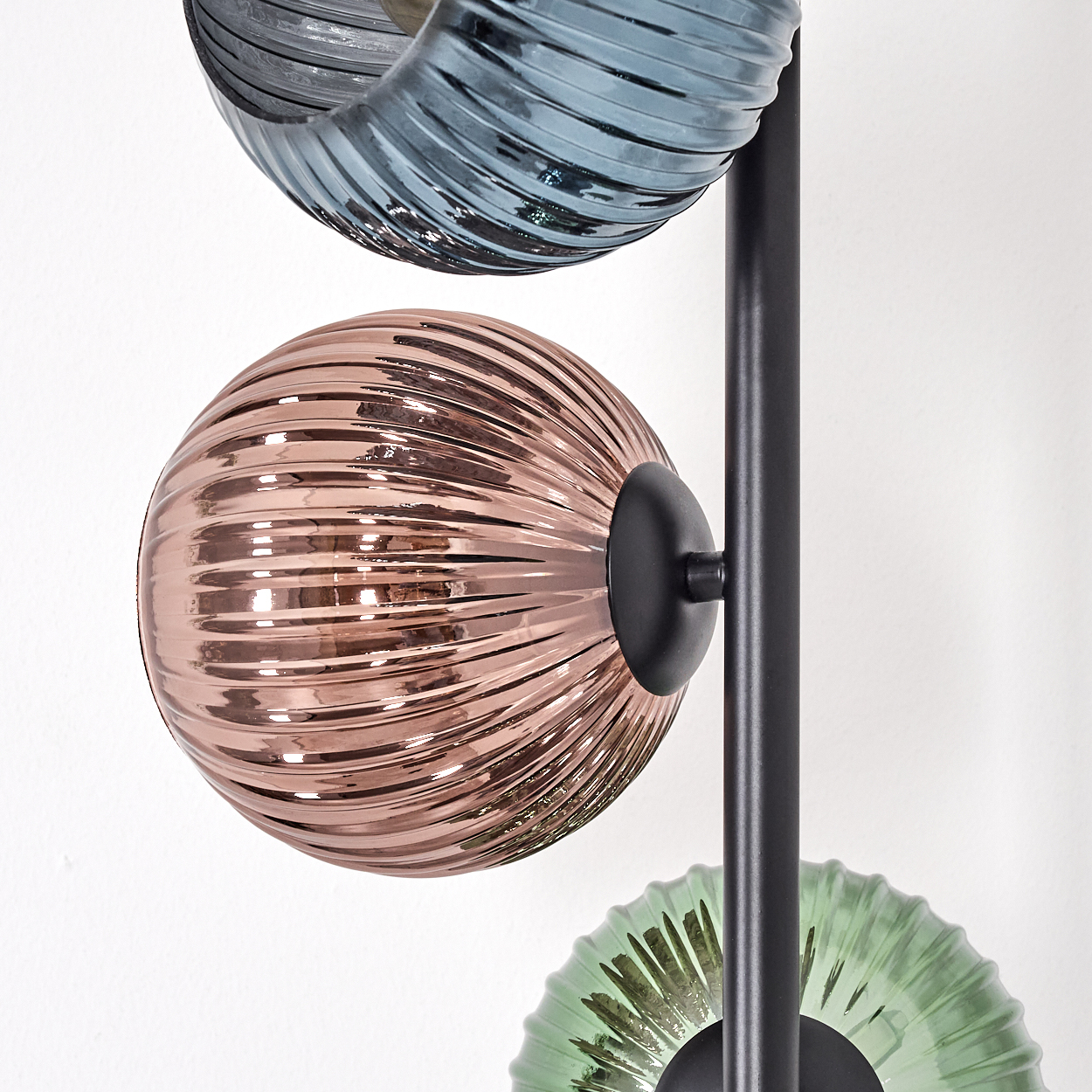 Eine moderne Lampe mit drei Glasschirmen in Blau, Roségold und Grün. Sie haben eine gerippte Textur und sind an einer schwarzen Stange befestigt.