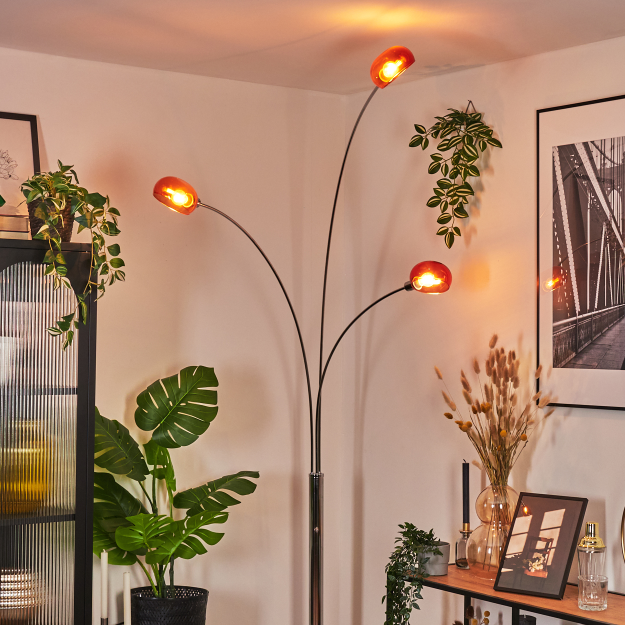 Ein modernes Wohnzimmer mit Stehlampe, Pflanzen, einem gerahmten Bild und einem Beistelltisch. Die Lampe hat orangefarbene Kugeln.