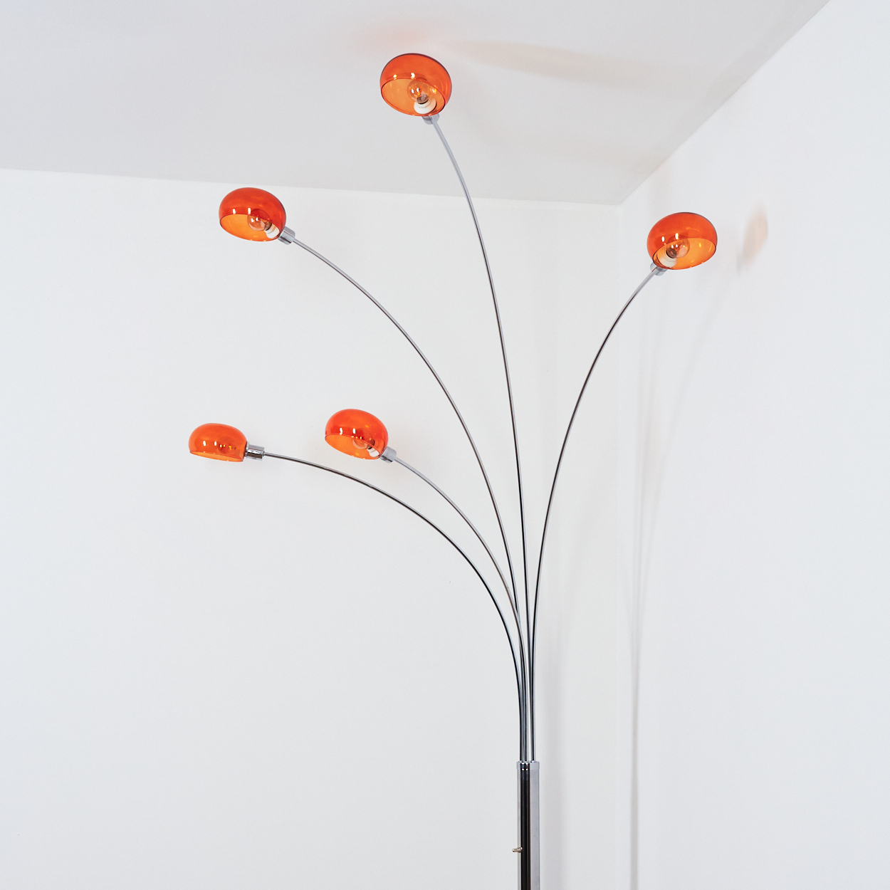 Eine moderne Stehlampe mit fünf orangefarbenen Lampenschirmen. Die Lampe hat einen Chromstiel und gebogene Arme vor einer weißen Wand.