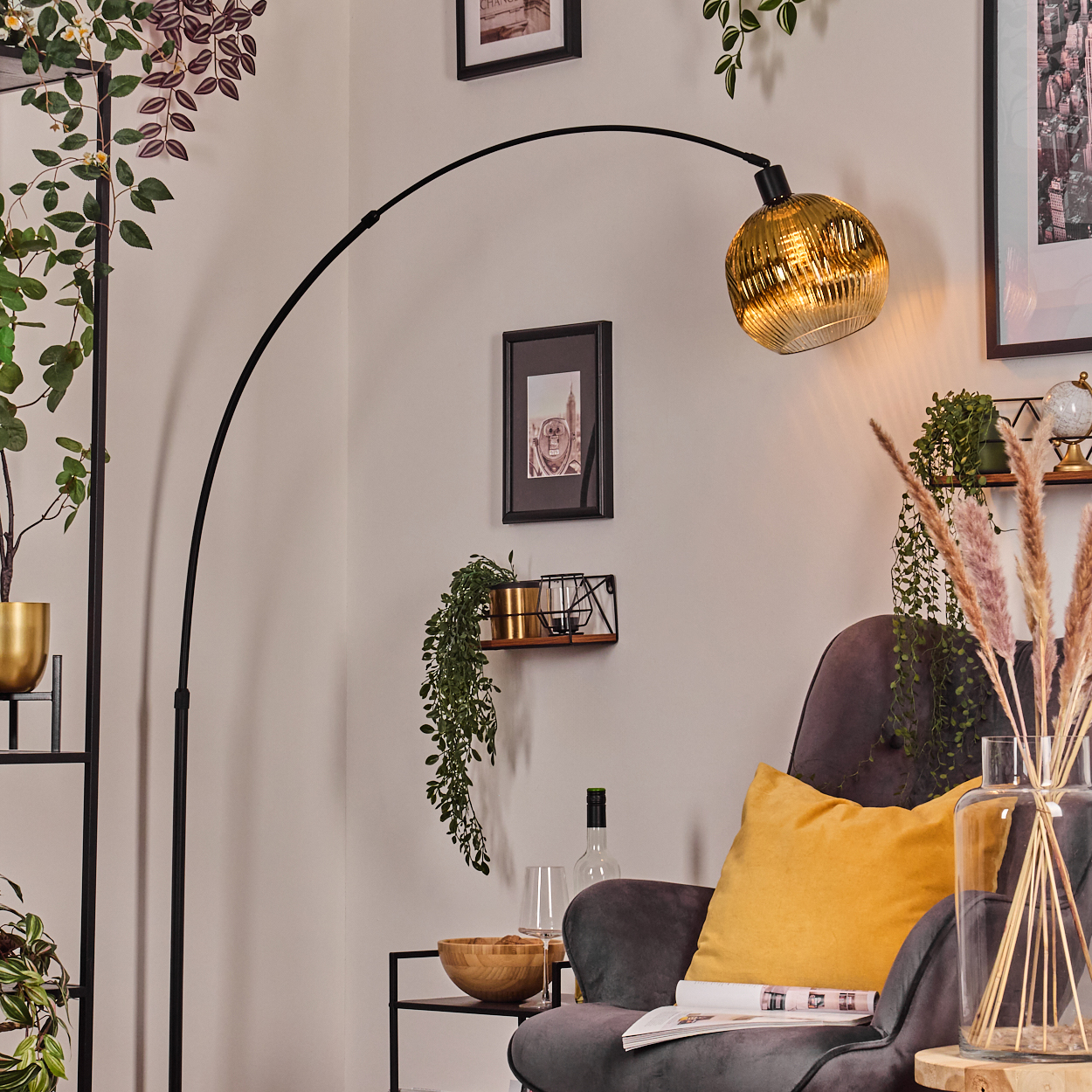 Ein modernes Wohnzimmer mit einer schwarzen Bogenlampe. Ein grauer Sessel hat ein gelbes Kissen. Pflanzen und gerahmte Bilder schmücken die Wände.