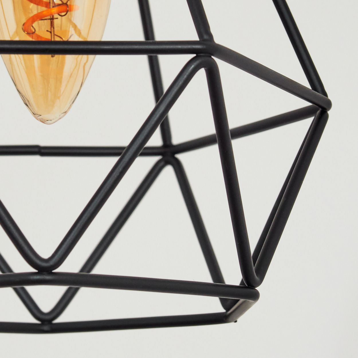 Nahaufnahme eines schwarzen geometrischen Lampenschirms mit einer warm getönten Glühbirne. Der Hintergrund ist weiß.