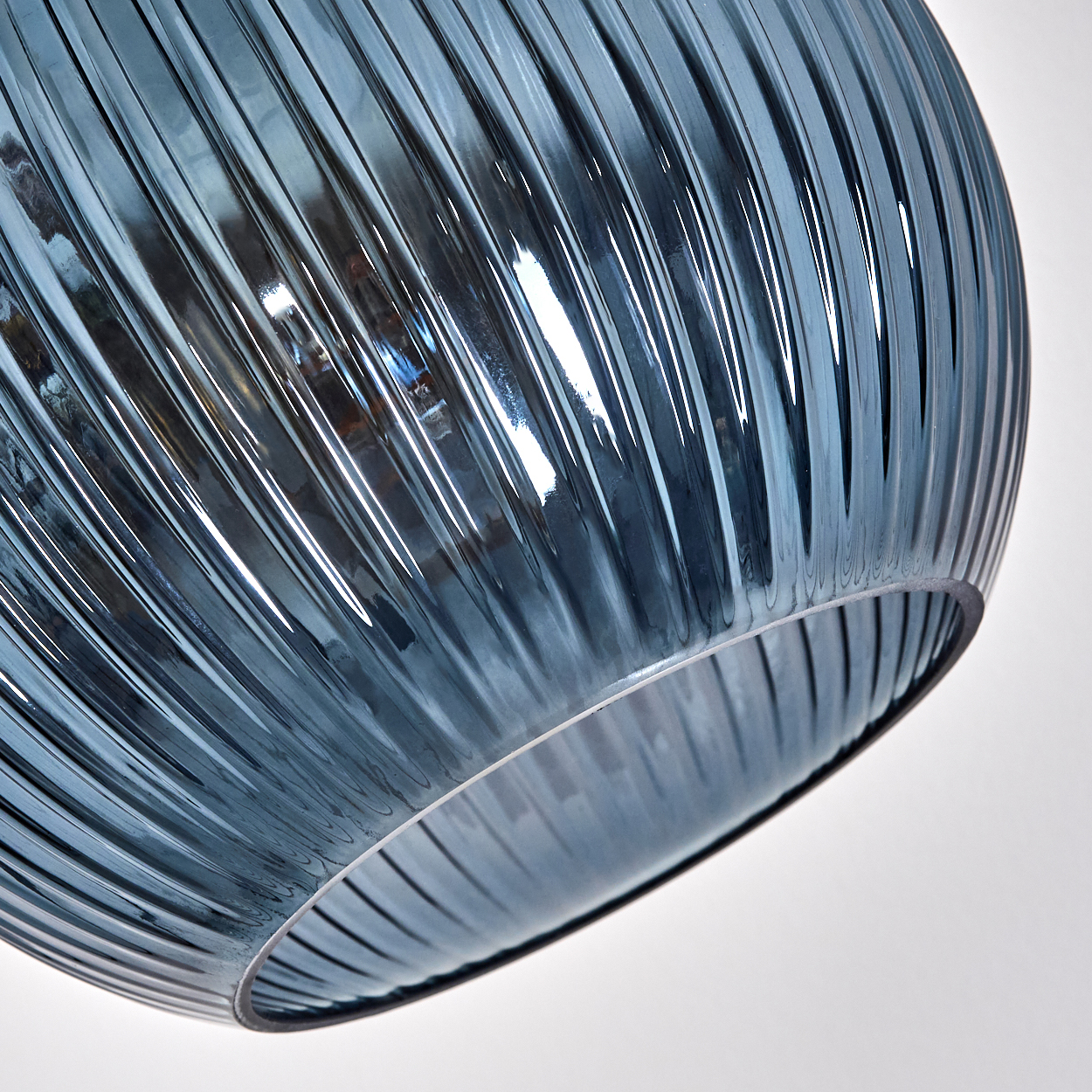 Nahaufnahme eines blauen Glaslampenschirms mit vertikalen Rippen. Der Hintergrund ist weiß, das Glas reflektiert das Licht.
