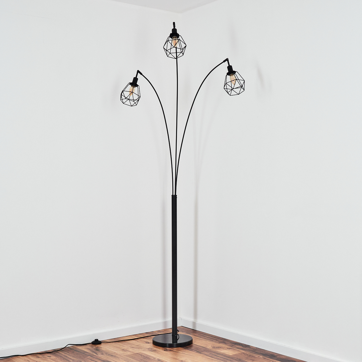 Eine schwarze Stehlampe mit drei Lichtern. Sie steht in einer Ecke mit weißen Wänden und Holzboden.