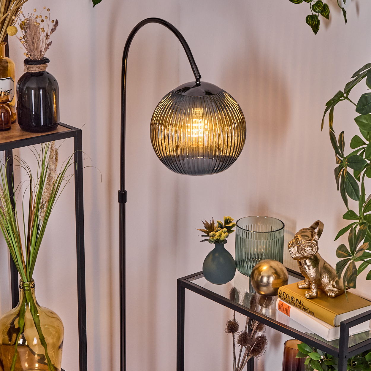 Ein modernes Wohnzimmer mit schwarzer Stehlampe, Glasregalen und Dekorationen wie Pflanzen und goldener Hundestatue.