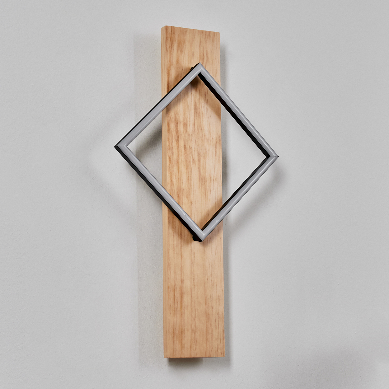 Ein Holzbrett mit einem schwarzen und silbernen quadratischen Rahmen. Der Hintergrund ist eine schlichte weiße Wand.
