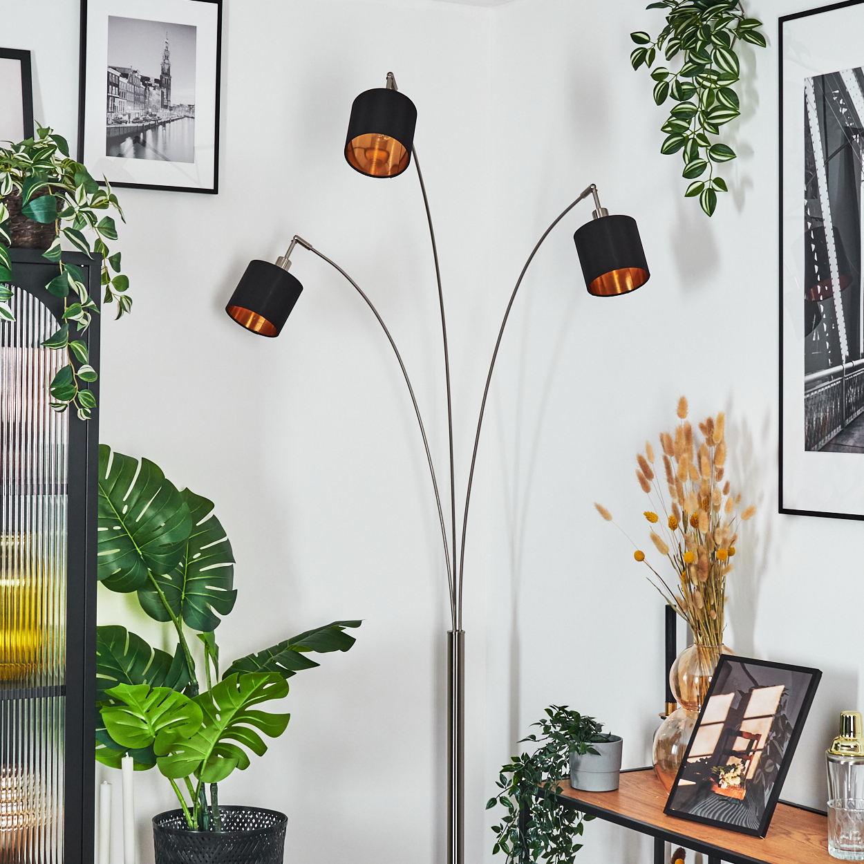 Ein modernes Wohnzimmer mit einer schwarz-goldenen Stehlampe, Pflanzen, gerahmten Bildern und einem Holzregal.