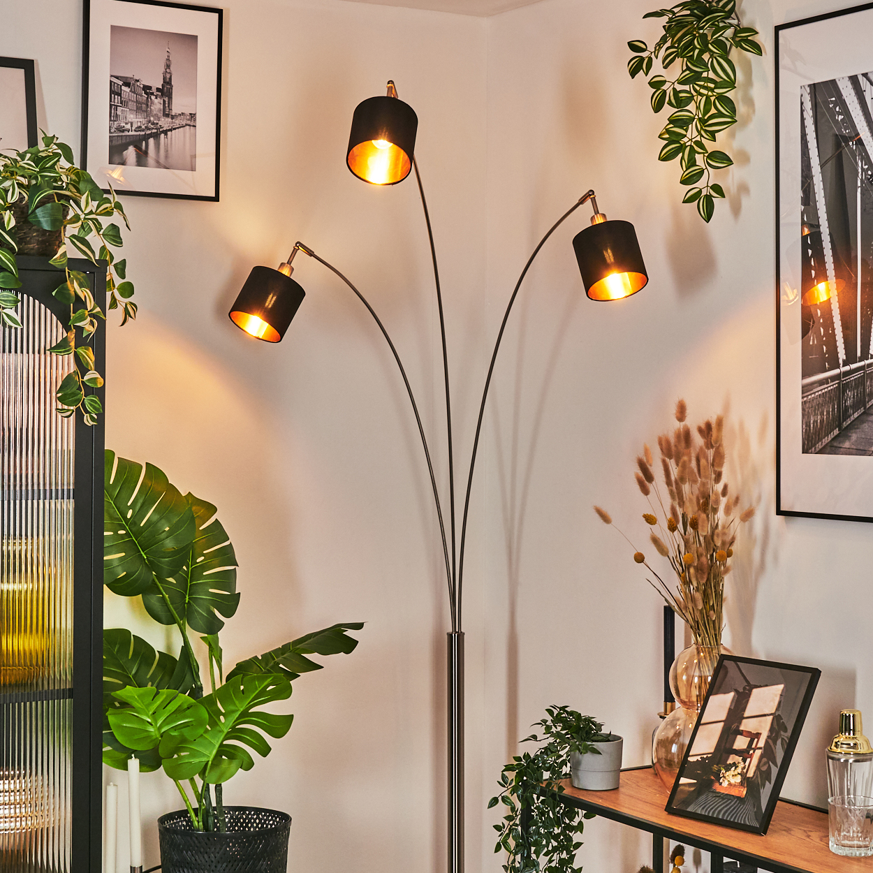 Ein modernes Wohnzimmer mit schwarzer Stehlampe, Pflanzen, gerahmten Bildern und einem Holzregal.