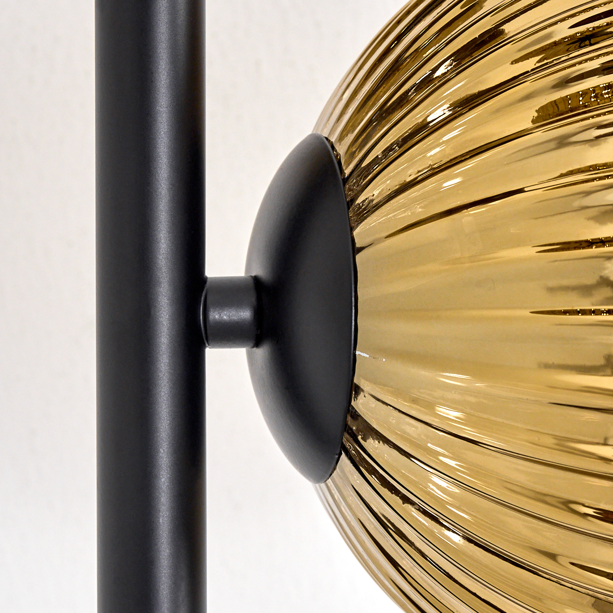Nahaufnahme einer Lampe. Schwarzer Metallschaft und Halterung. Bernsteinfarbene Glaskugel mit vertikalen Rippen. Weißer Hintergrund.