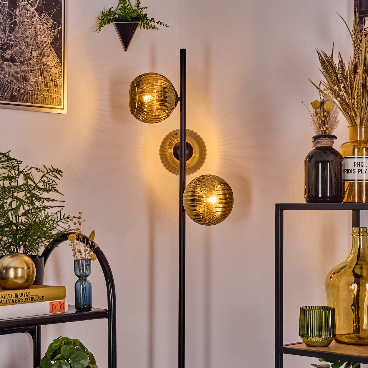Moderne Zimmerecke mit schwarzer Lampe mit goldenen Kugeln, Regalen mit Dekorationen, einer Karte und Pflanzen.