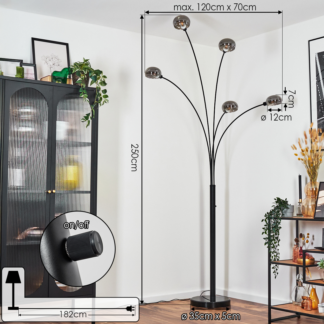Eine schwarze Stehlampe mit fünf Lichtern. Sie hat einen runden Fuß und einen schwarzen Metallrahmen. Im Hintergrund steht ein schwarzer Schrank.