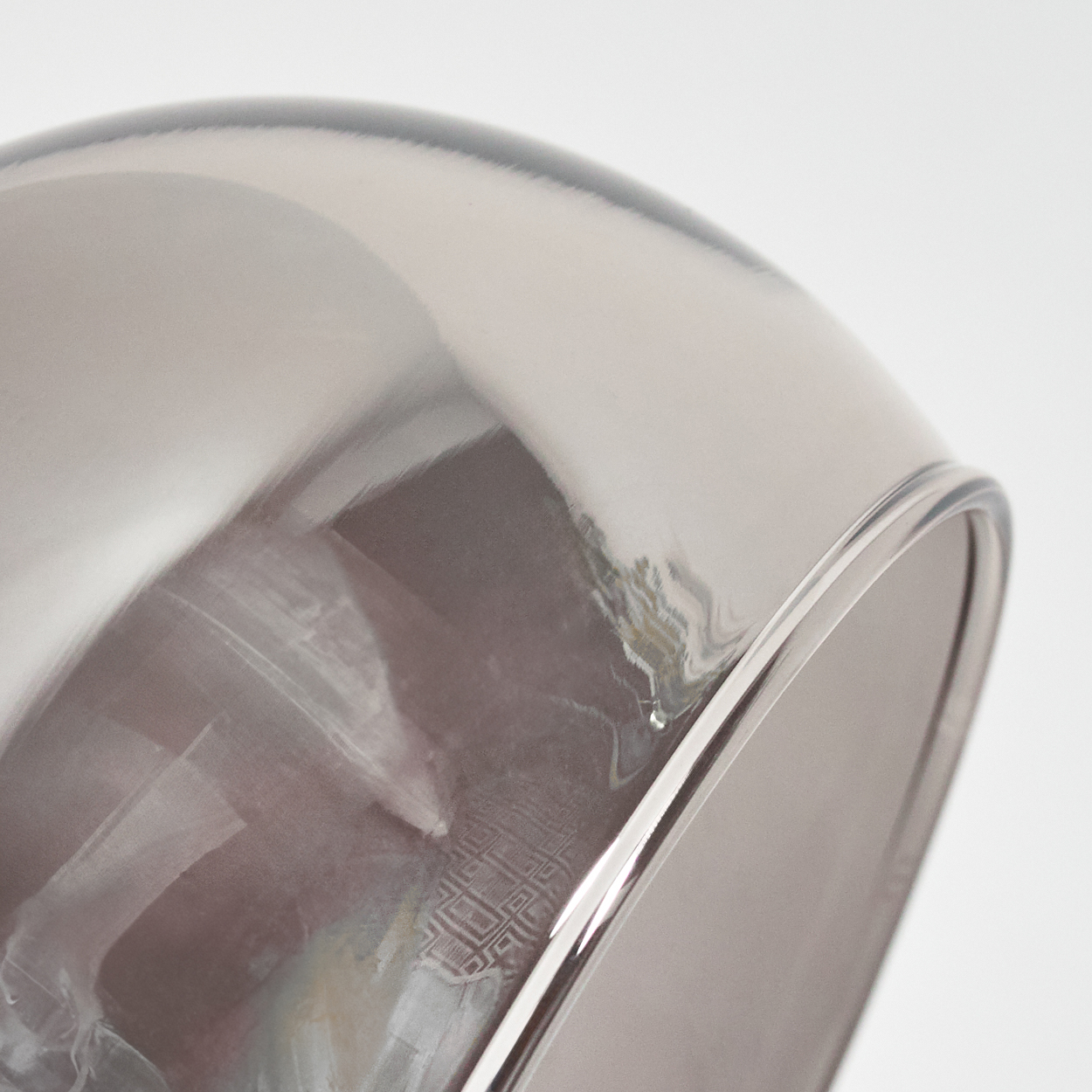 Nahaufnahme einer Glasschale mit glänzender, reflektierender Oberfläche. Die Schale ist grau und klar und spiegelt ein Muster im Inneren wider.