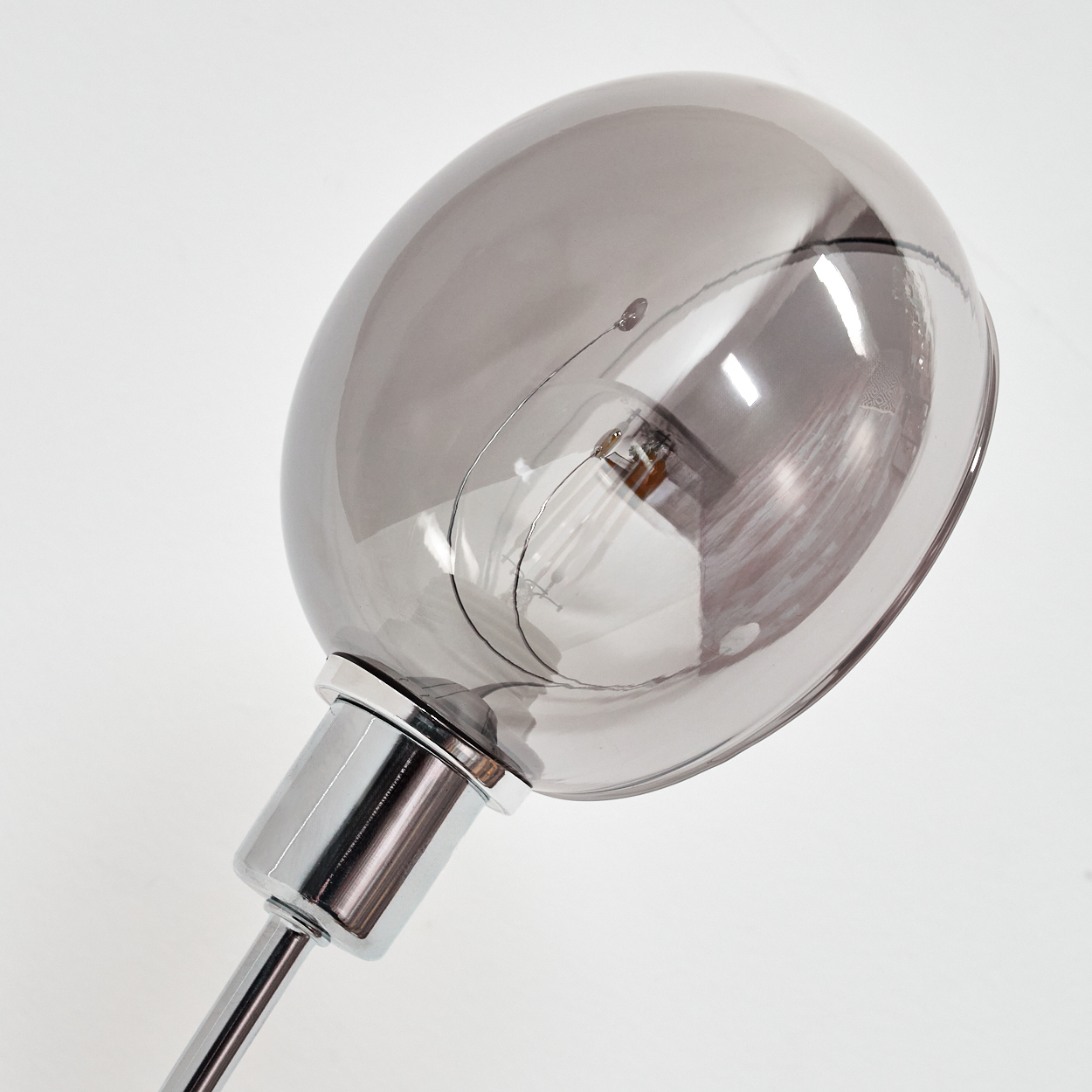Nahaufnahme einer stilvollen Lampe mit grauer Glühbirne und Chromfuß, vor weißem Hintergrund.