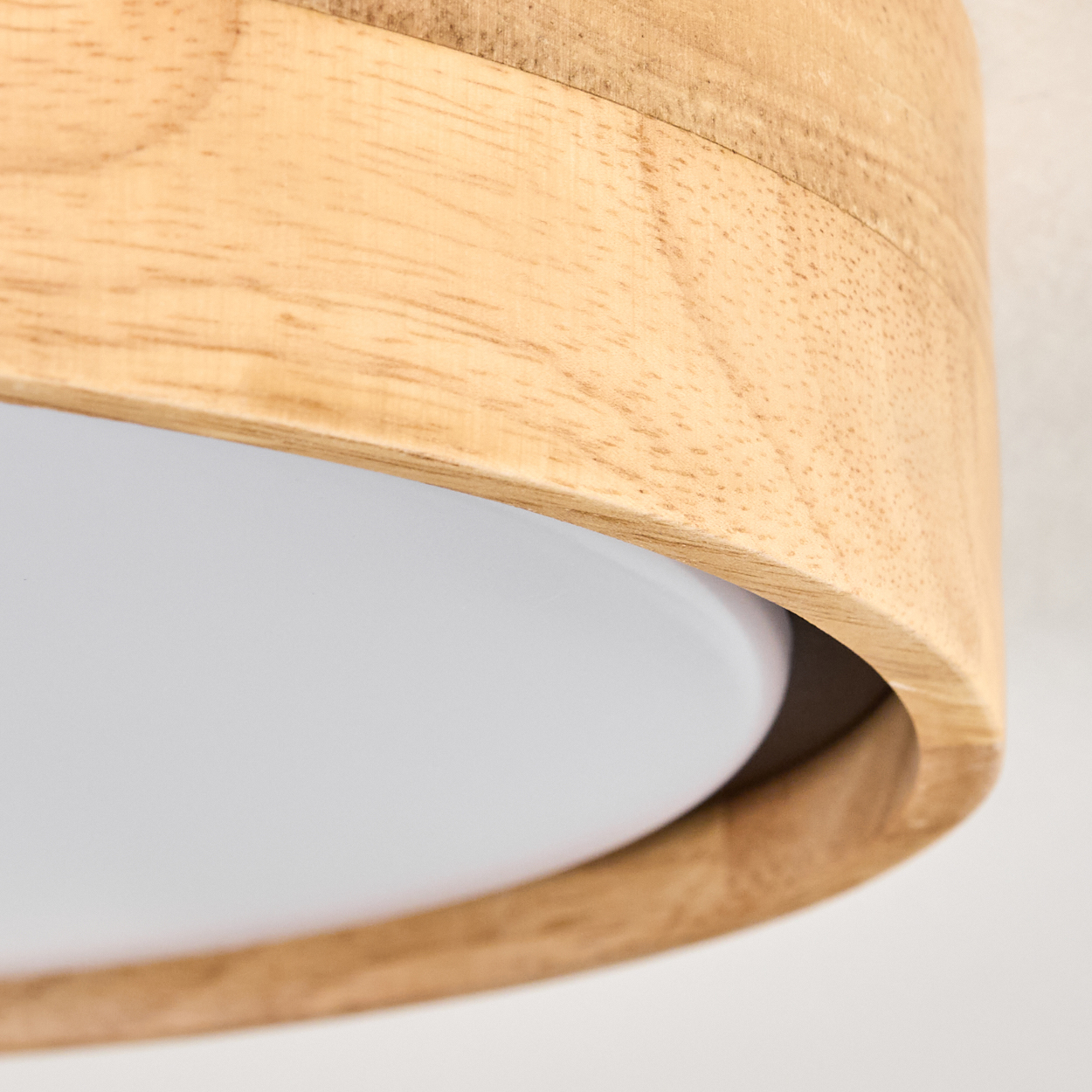 Nahaufnahme einer Holzlampe. Ein heller Holzrahmen umgibt eine weiße Lichttafel. Der Hintergrund ist eine weiße Wand.