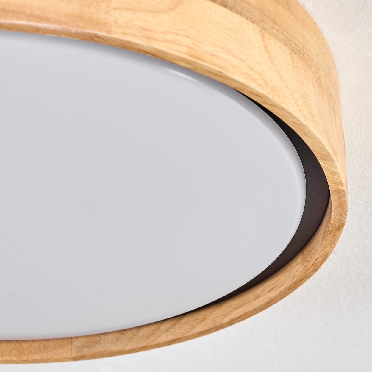 Nahaufnahme einer Holzgerahmten Deckenleuchte mit ovalförmiger, weißer Lichtquelle vor weißer Wand.