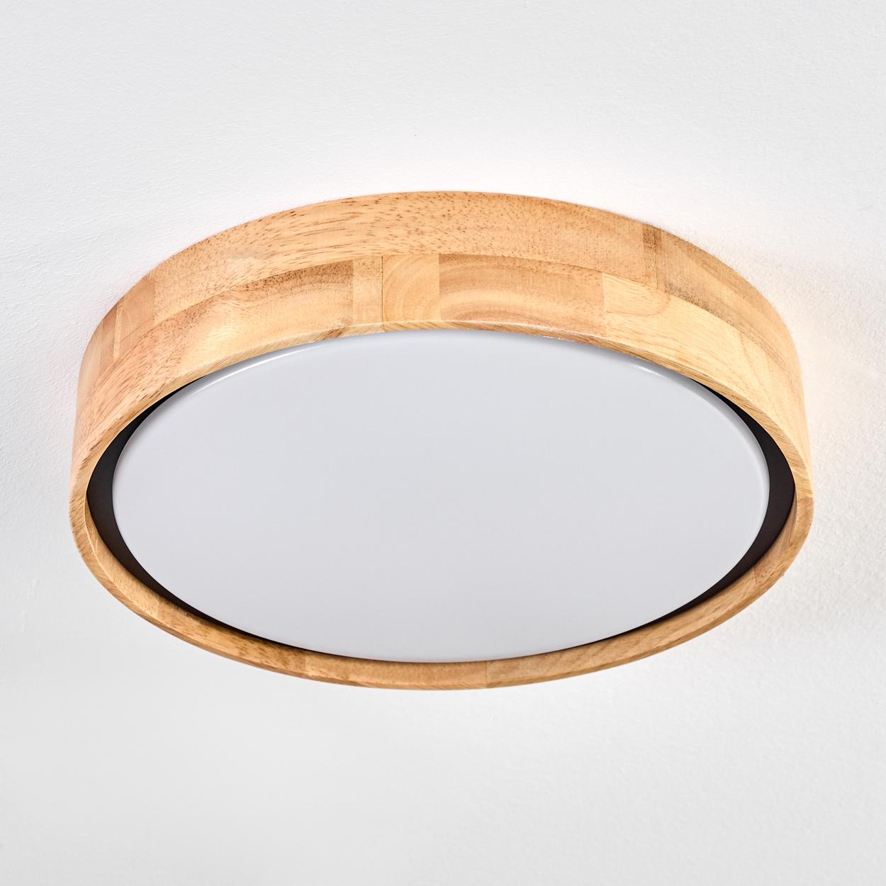 Eine runde Deckenleuchte aus Holz mit einer weißen, kreisförmigen Lichtfläche. Die Lampe ist an einer weißen Decke montiert.