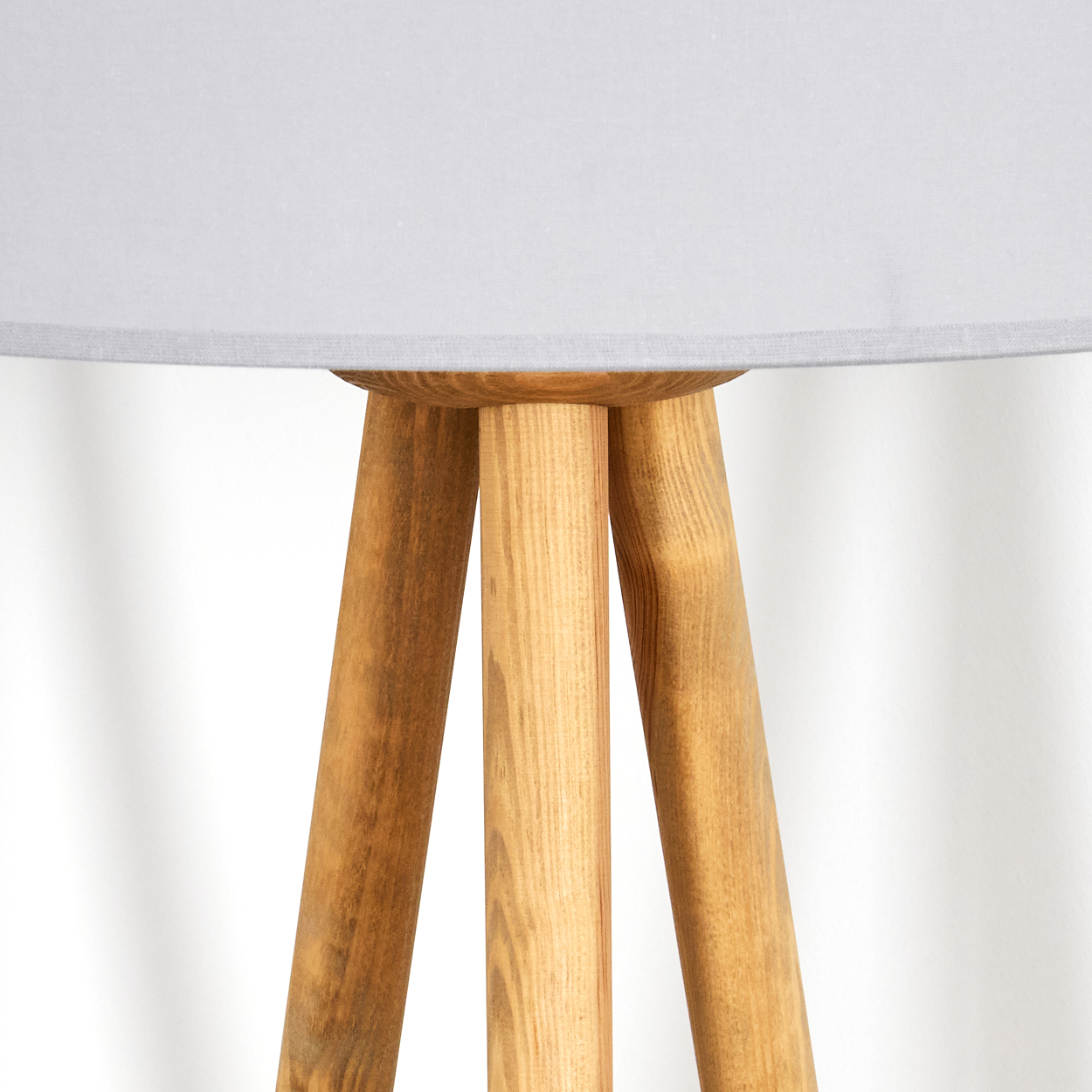 Nahaufnahme eines hölzernen Stativ-Lampenfußes mit grauem Lampenschirm. Die Holzbeine sind braun und tragen den Lampenschirm.