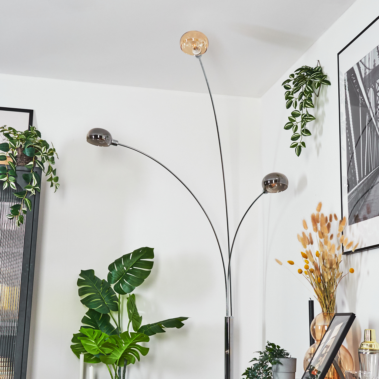 Eine moderne Stehlampe mit drei kugelförmigen Schirmen. Pflanzen und gerahmte Kunst umgeben die Lampe.