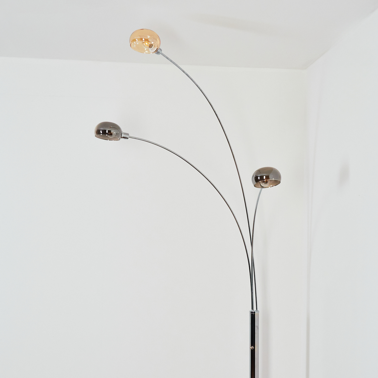 Eine moderne Stehlampe mit drei gebogenen Armen, die jeweils eine Kugellampe tragen. Der Sockel ist schwarz und verchromt. Der Hintergrund ist weiß.