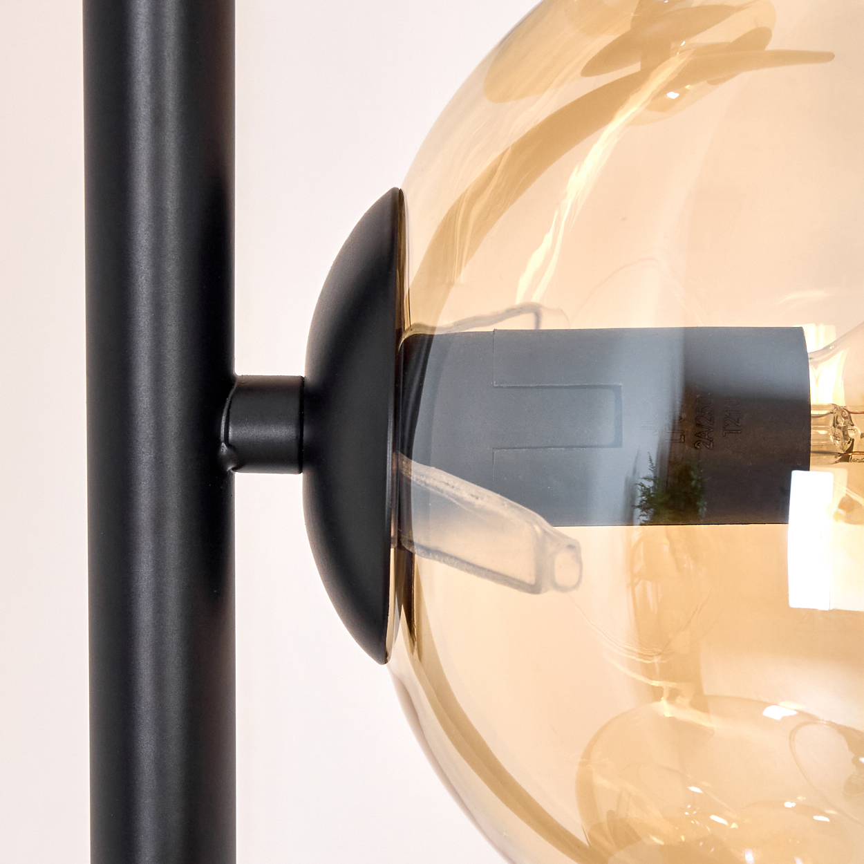Nahaufnahme einer schwarzen Lampe mit einer klaren, bernsteinfarbenen Glühbirne. Links ist ein schwarzer Pfosten. Die Glühbirne leuchtet.