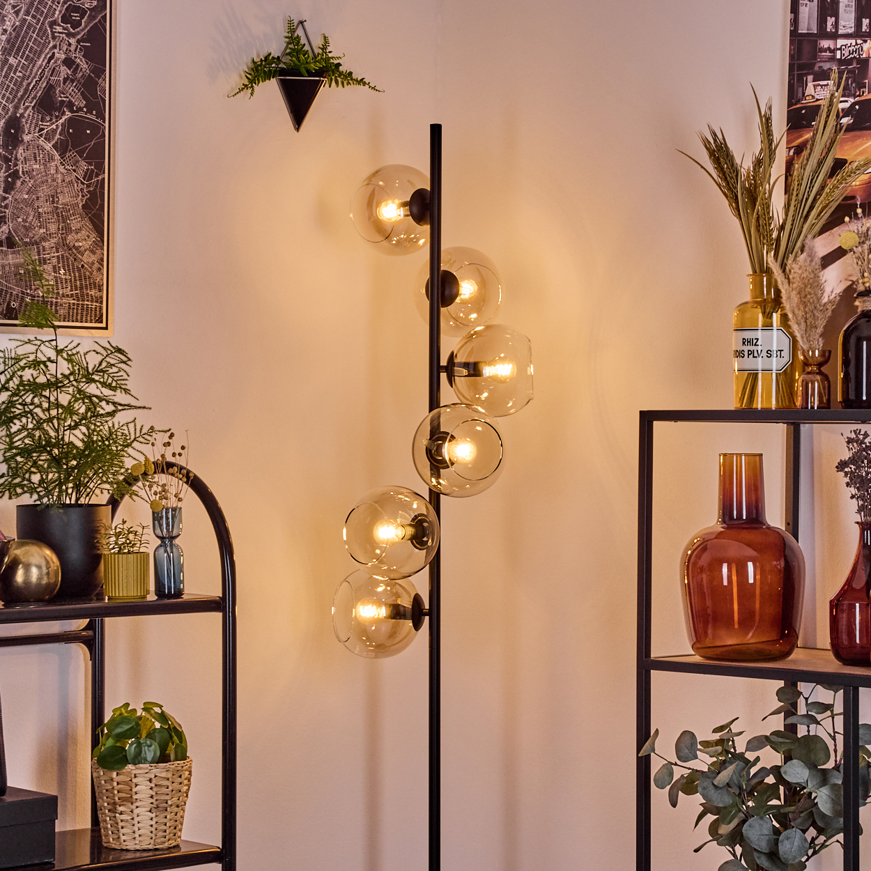 Ein modernes Wohnzimmer mit einer schwarzen Stehlampe mit Glaskugeln. Regale mit Pflanzen und Dekorationsgegenständen sind sichtbar.
