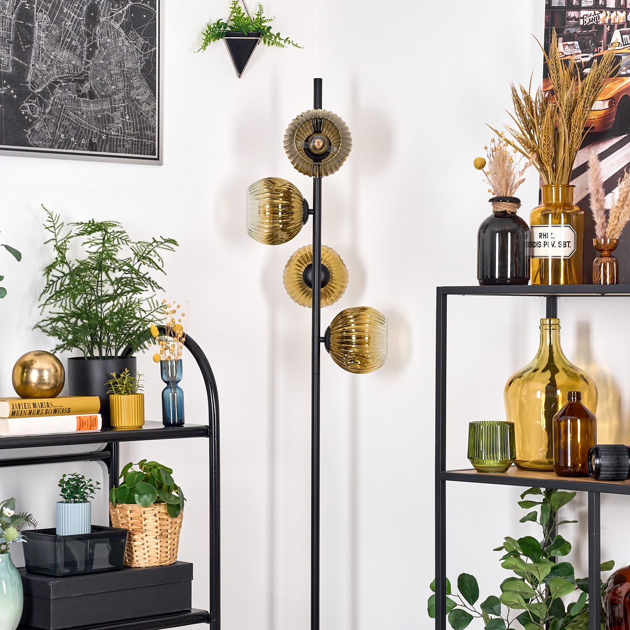 Ein Raum mit einem schwarzen Metallregal, Pflanzen, einer Stehlampe mit goldenen Lampenschirmen und dekorativen Flaschen.