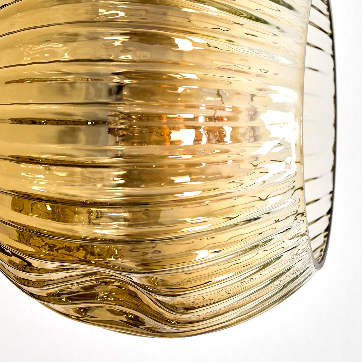 Nahaufnahme eines goldenen, gerippten Glasobjekts. Licht reflektiert von der gewölbten Oberfläche. Der Hintergrund ist weiß.