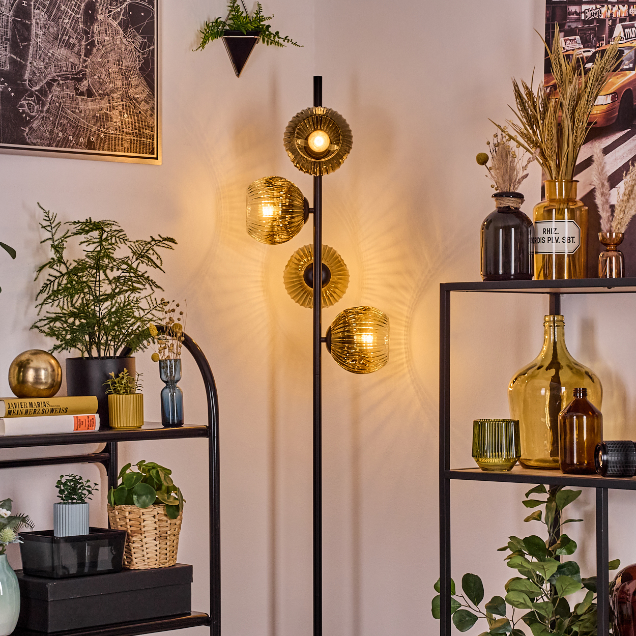 Eine Zimmerecke mit einer schwarzen Stehlampe, Regalen mit Pflanzen und Vasen und einem Kartenaufdruck an der Wand.