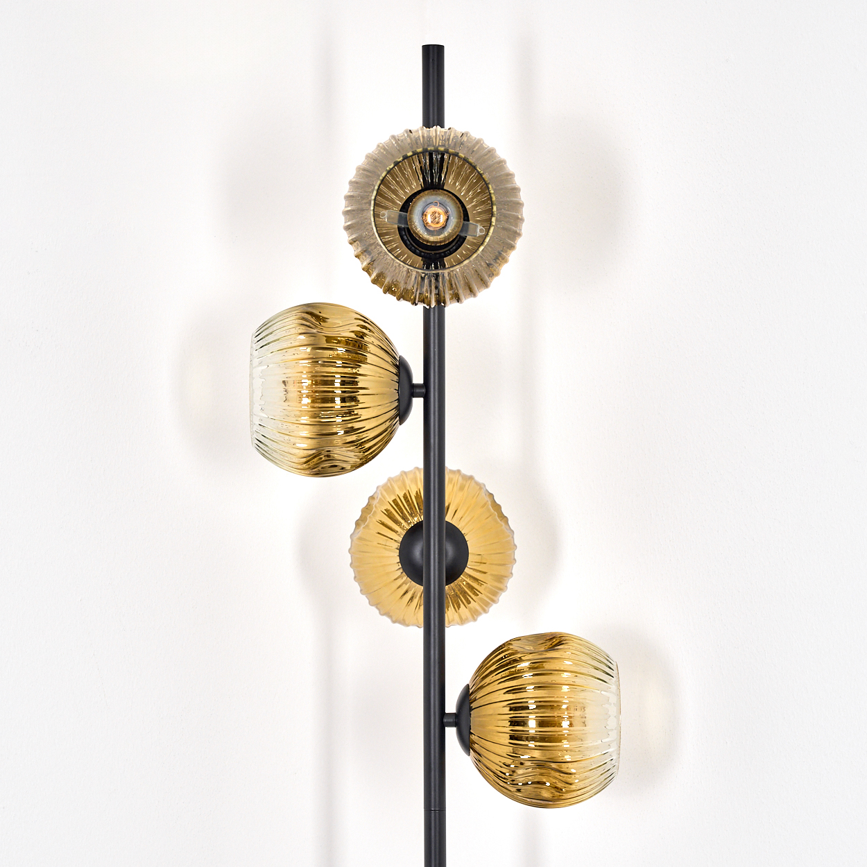 Eine moderne Wandleuchte mit drei goldenen Glasschirmen und zwei goldenen kreisförmigen Elementen auf einem schwarzen Metallrahmen.