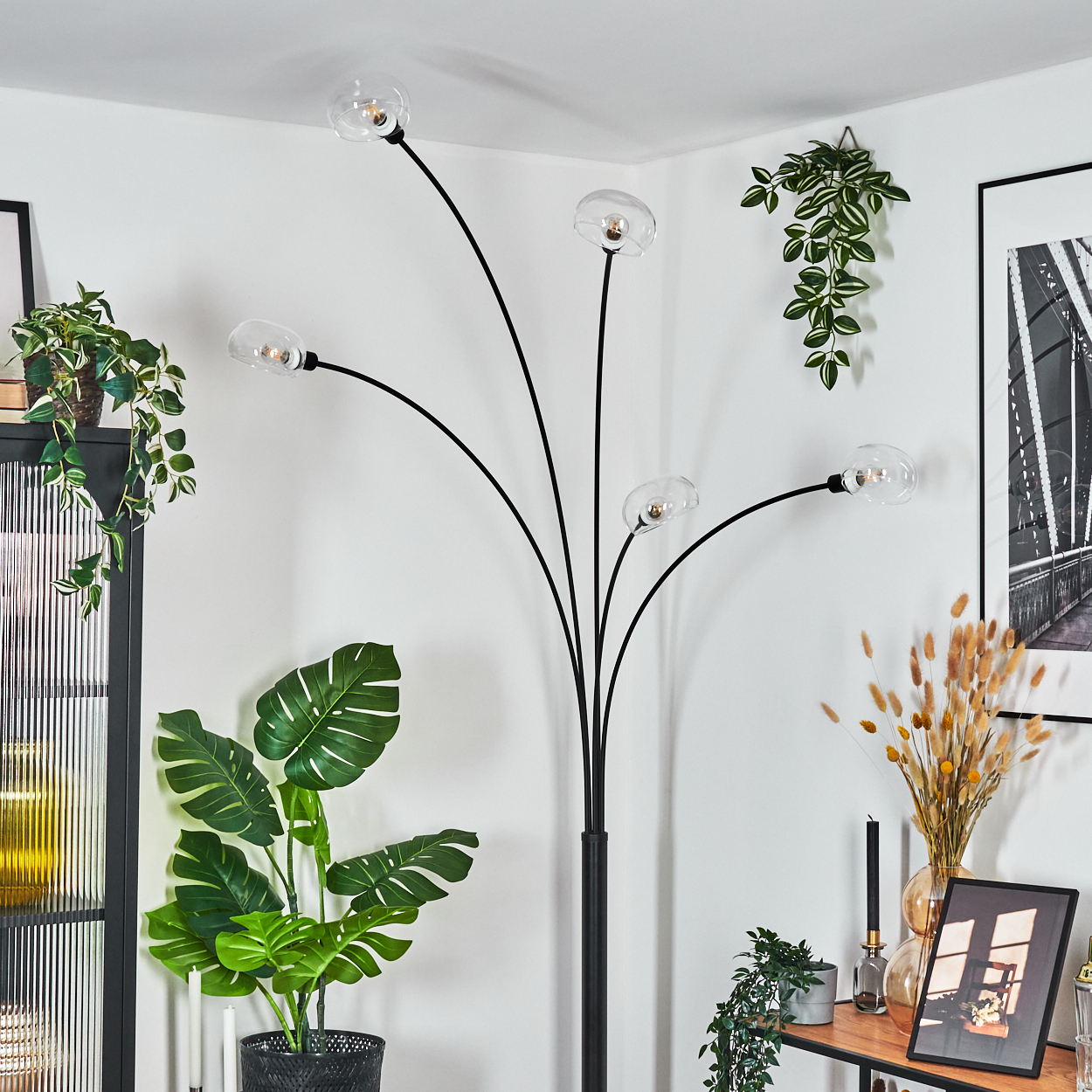 Ein modernes Wohnzimmer mit schwarzer Stehlampe, Pflanzen und einem Holztisch mit Dekorationen. Die Wände sind weiß.