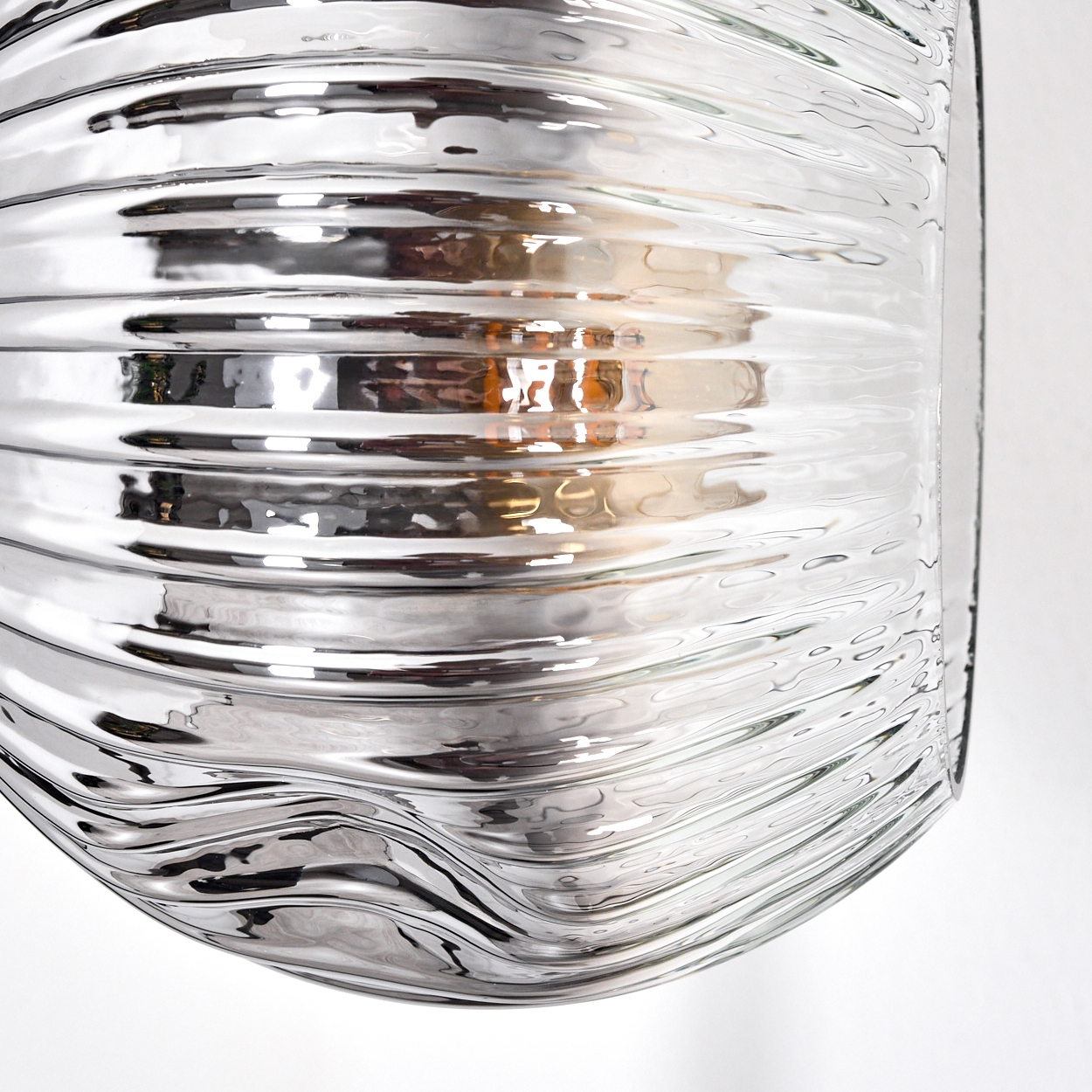 Nahaufnahme einer Glasleuchte mit gewellter Oberfläche, die das Licht reflektiert. Der Hintergrund ist weiß.