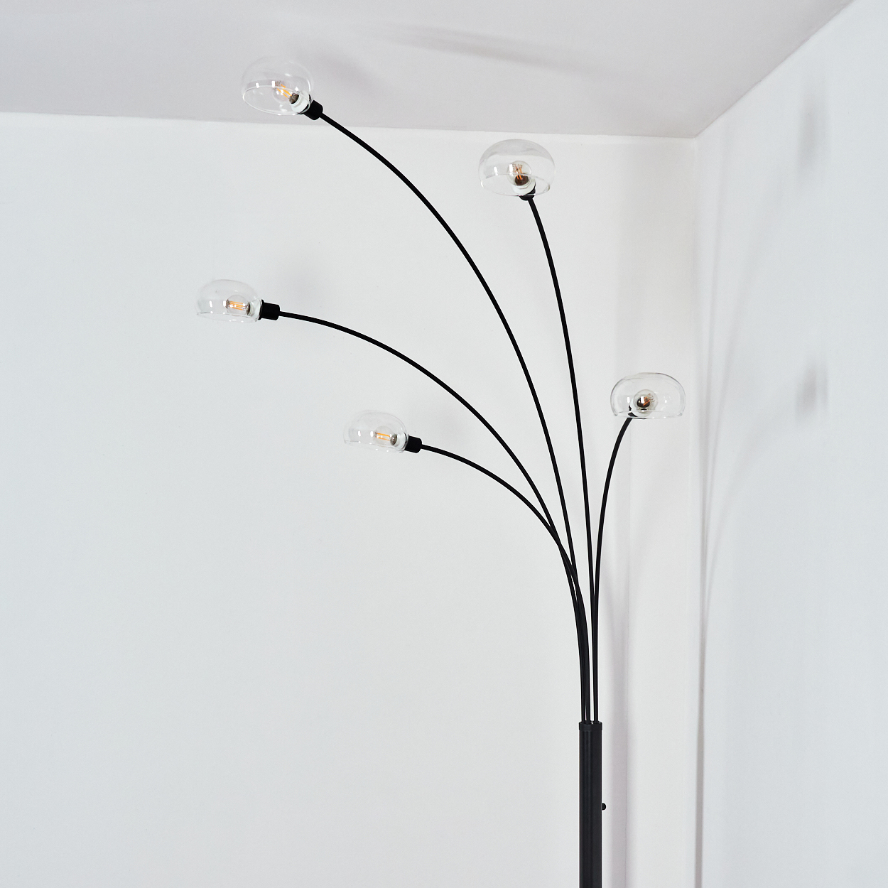 Eine moderne Stehlampe mit fünf gebogenen schwarzen Armen, die jeweils eine klare Glühbirne halten. Sie steht vor einer weißen Wand in einer Ecke.
