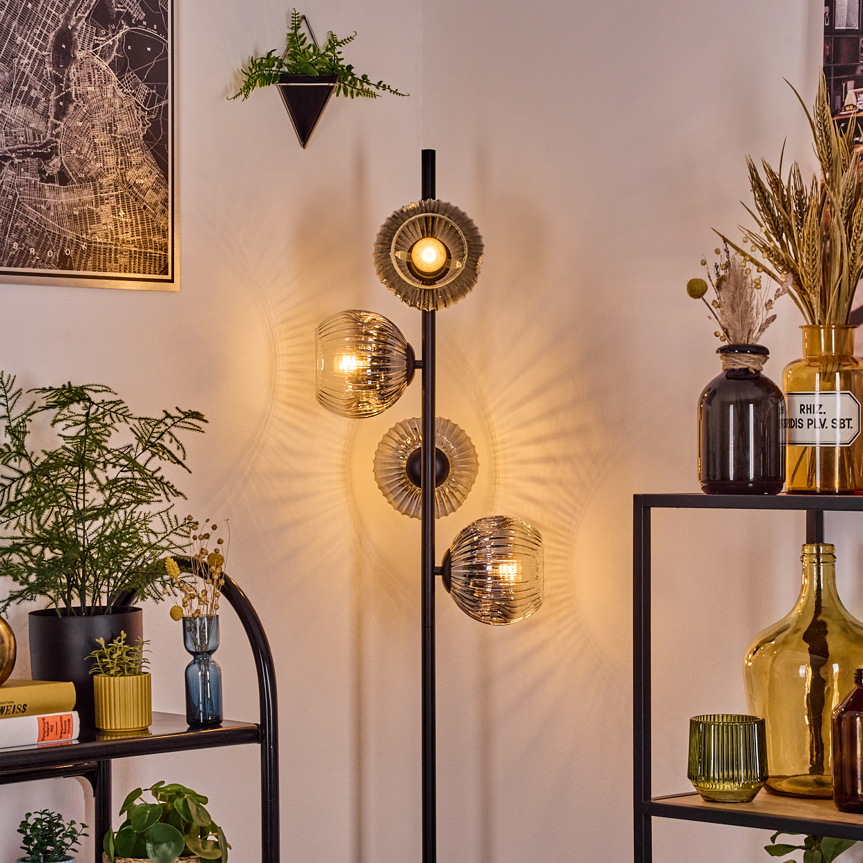 Ein modernes Wohnzimmer mit schwarzer Lampe, dekorativen Vasen, Pflanzen und einer Karte an der Wand. Die Lampe hat drei Glühbirnen.