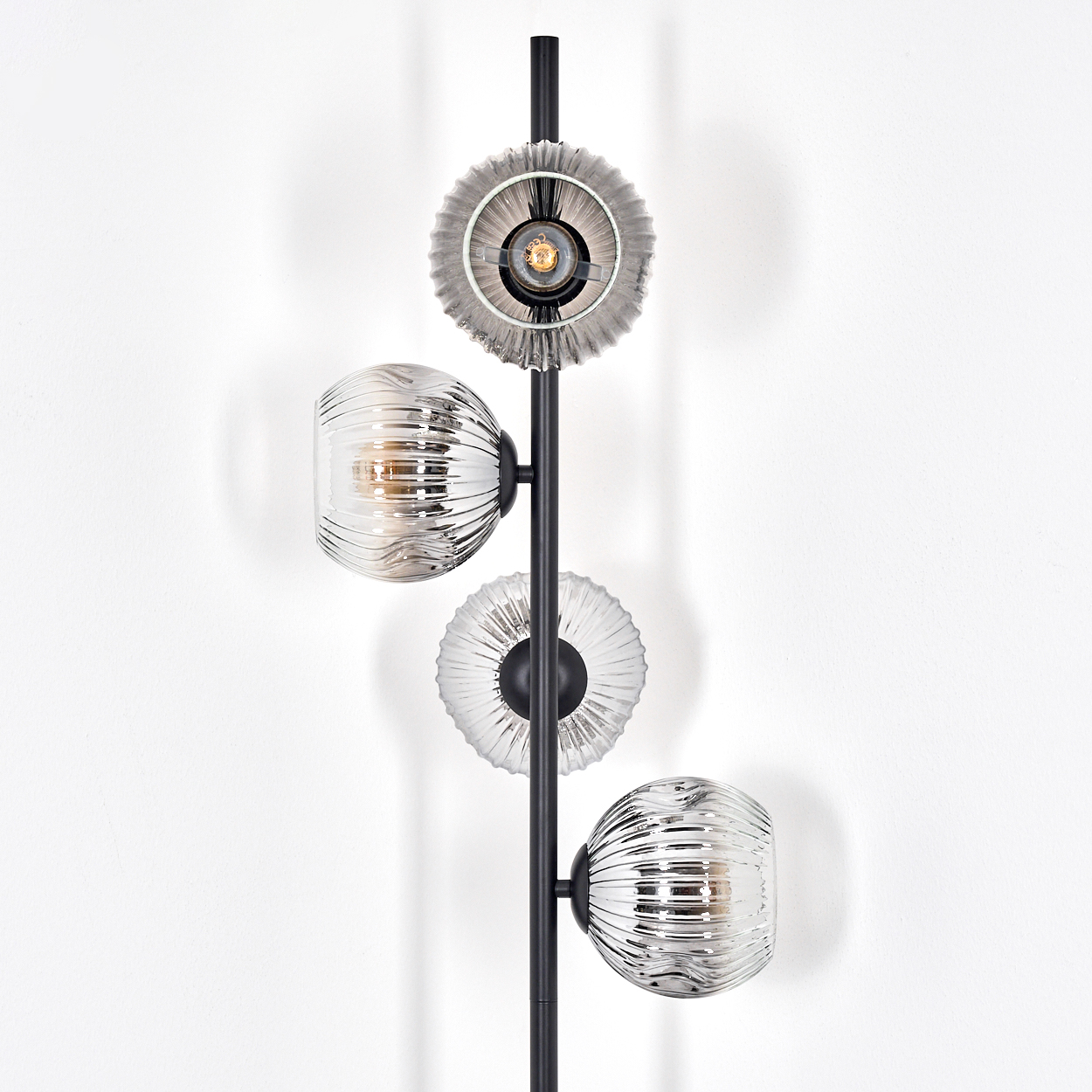 Eine moderne schwarze Stehlampe mit drei Glasschirmen und einer kreisförmigen Oberseite. Die Schirme sind gerippt und der Hintergrund ist weiß.