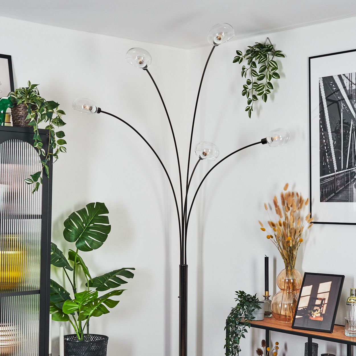 Eine moderne Stehlampe mit fünf Glaskugeln. Pflanzen und ein Regal mit Dekoration befinden sich in einem hellen Raum.