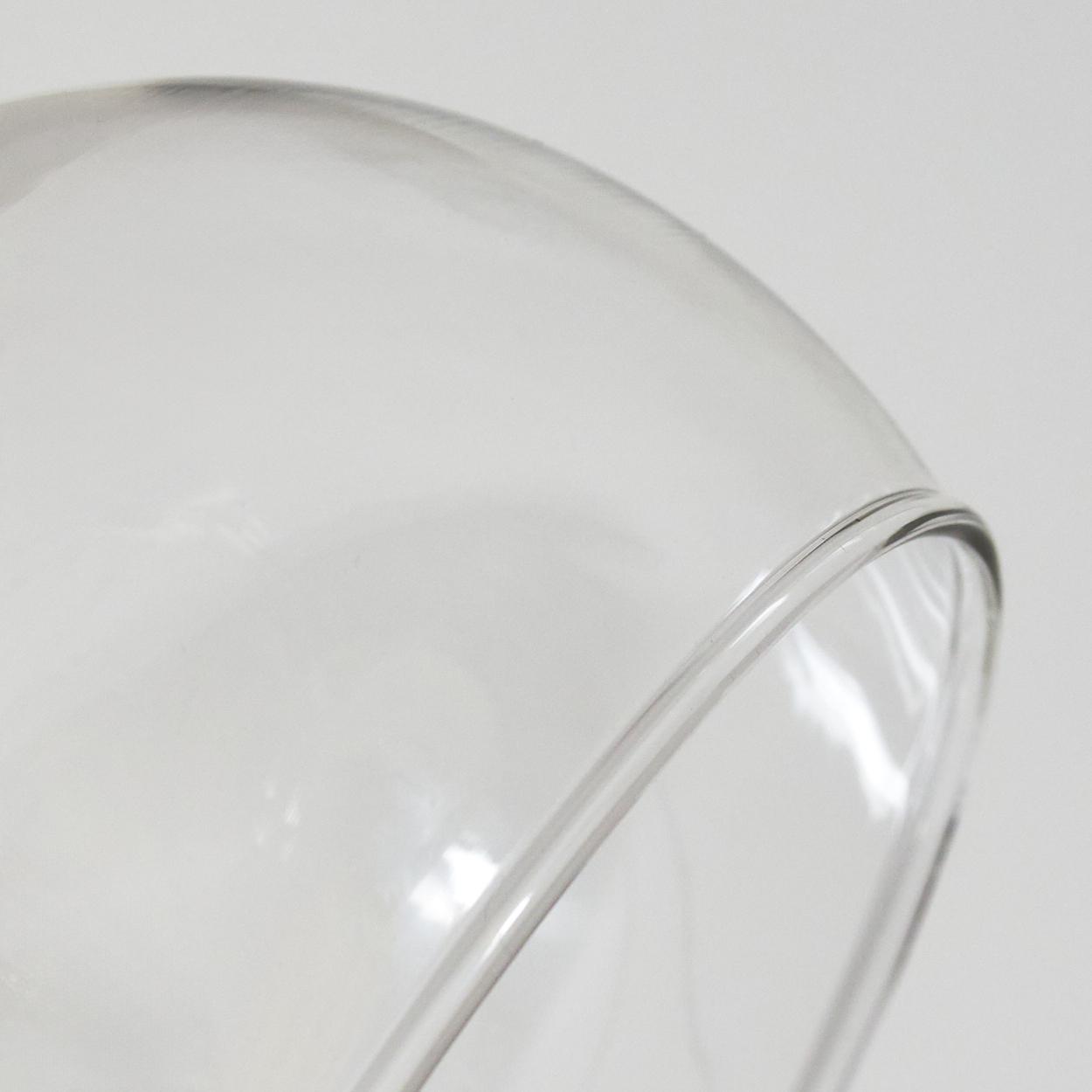 Nahaufnahme eines transparenten Glasobjekts mit gewölbtem Rand vor weißem Hintergrund. Das Glas ist klar.
