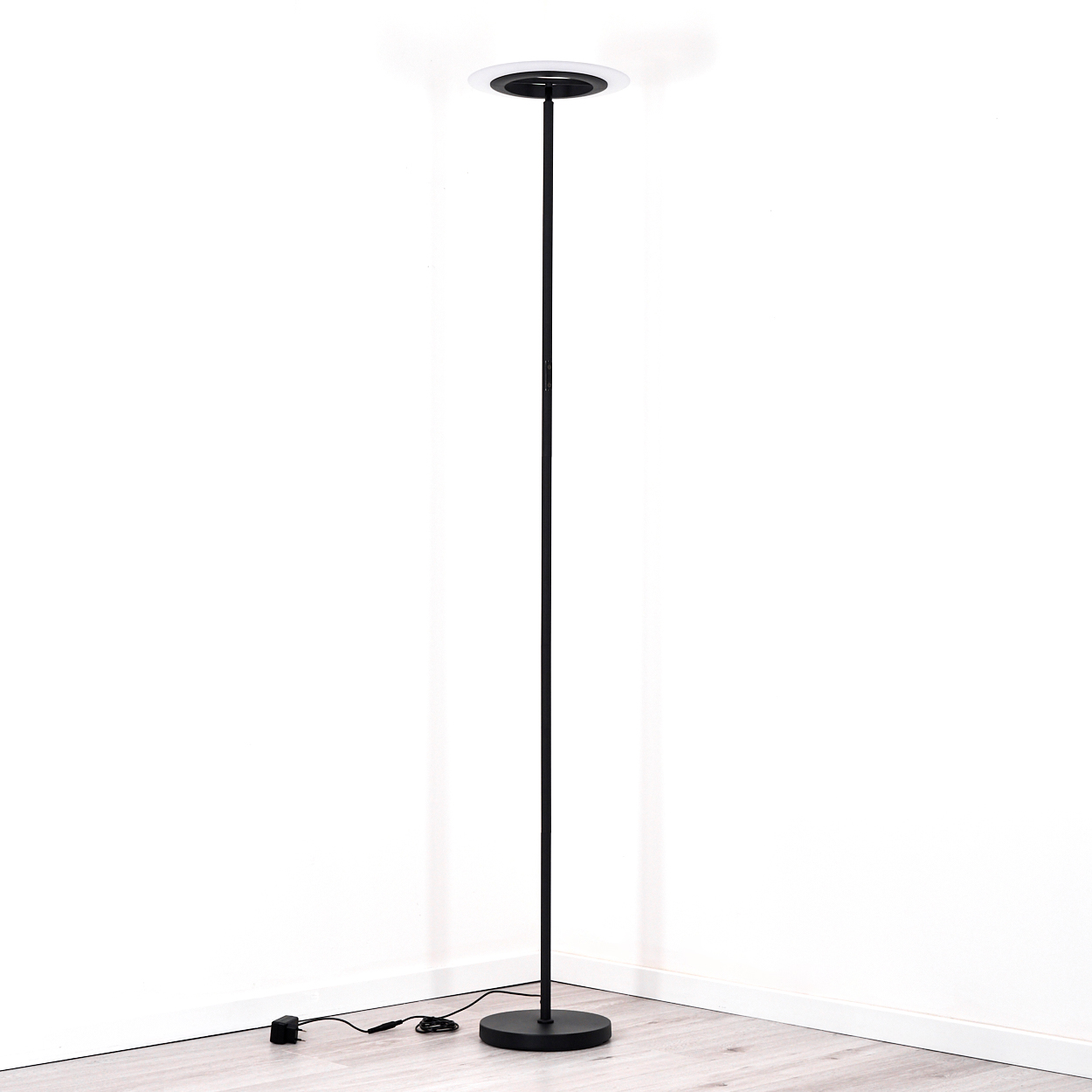 Eine moderne schwarze Stehlampe mit rundem Sockel und weißer Leuchte. Sie steht in der Ecke eines Raumes mit Holzboden.