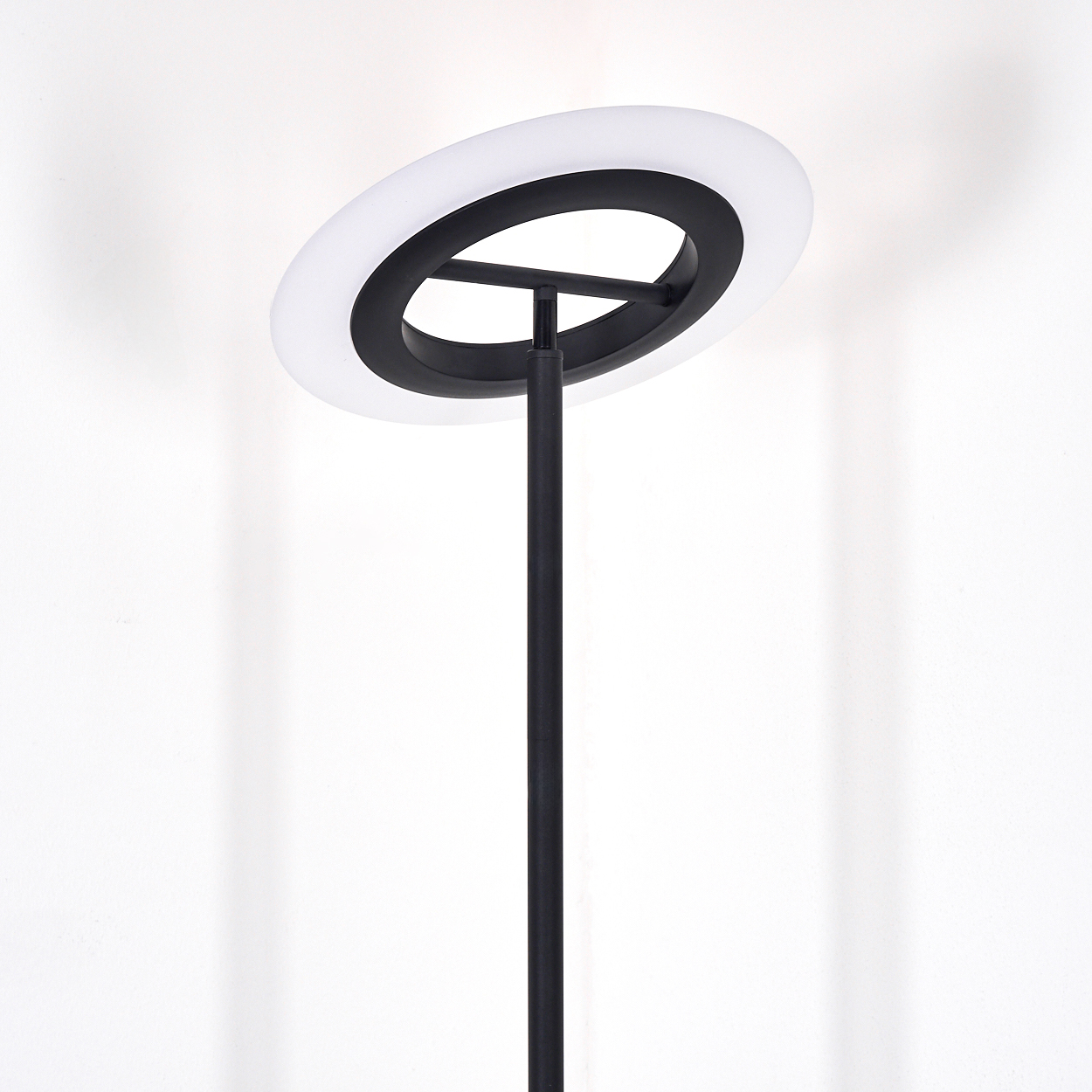 Eine moderne schwarze Stehlampe mit kreisförmigem Licht oben. Das Licht ist weiß, und der Hintergrund ist eine weiße Wand.